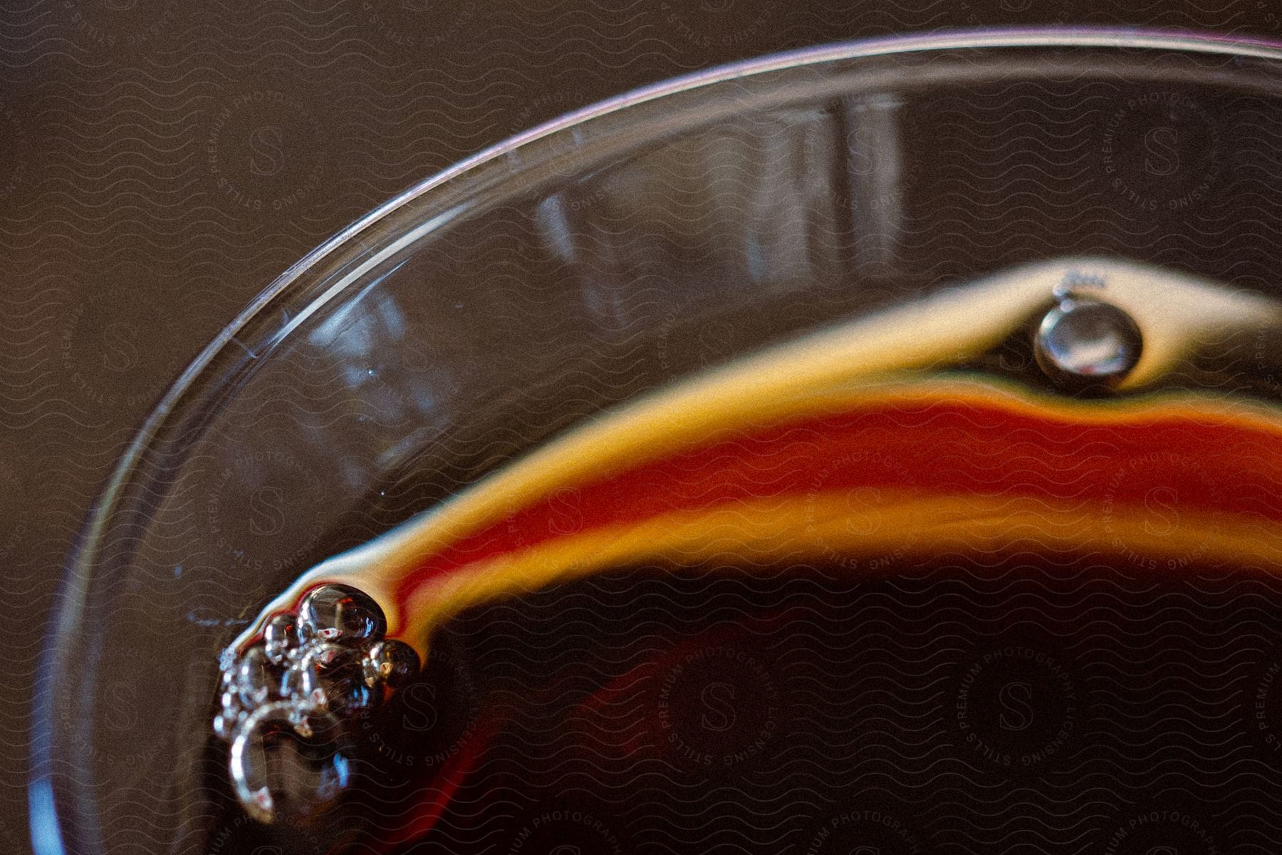 A close up of a black beverage in a clear glass cup with bubbles on the surface