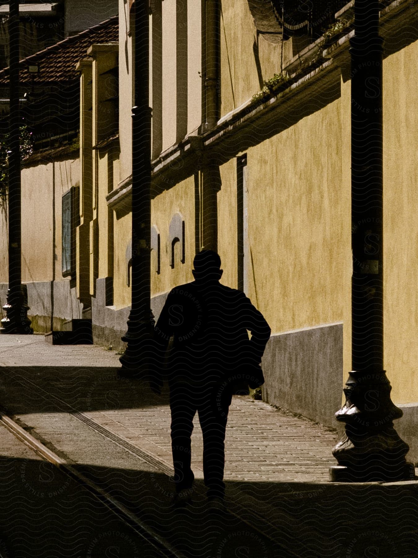 Man walking up the street is silhouetted at daytime in an urban setting