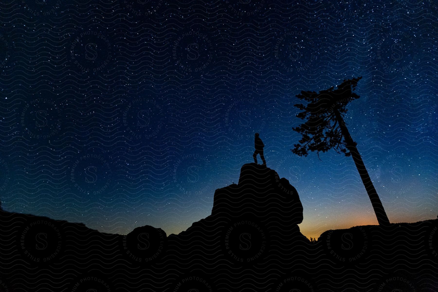 Silhouette of a man standing over a boulder under a starry sky