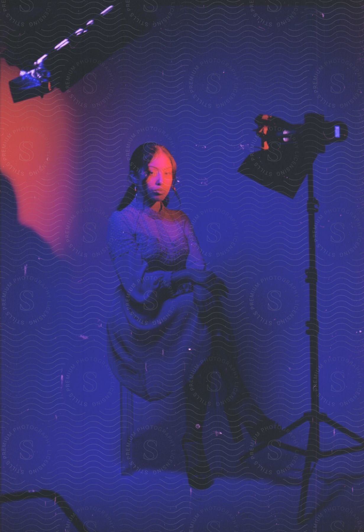 A young woman in a dress poses in red lighting against a blue background.