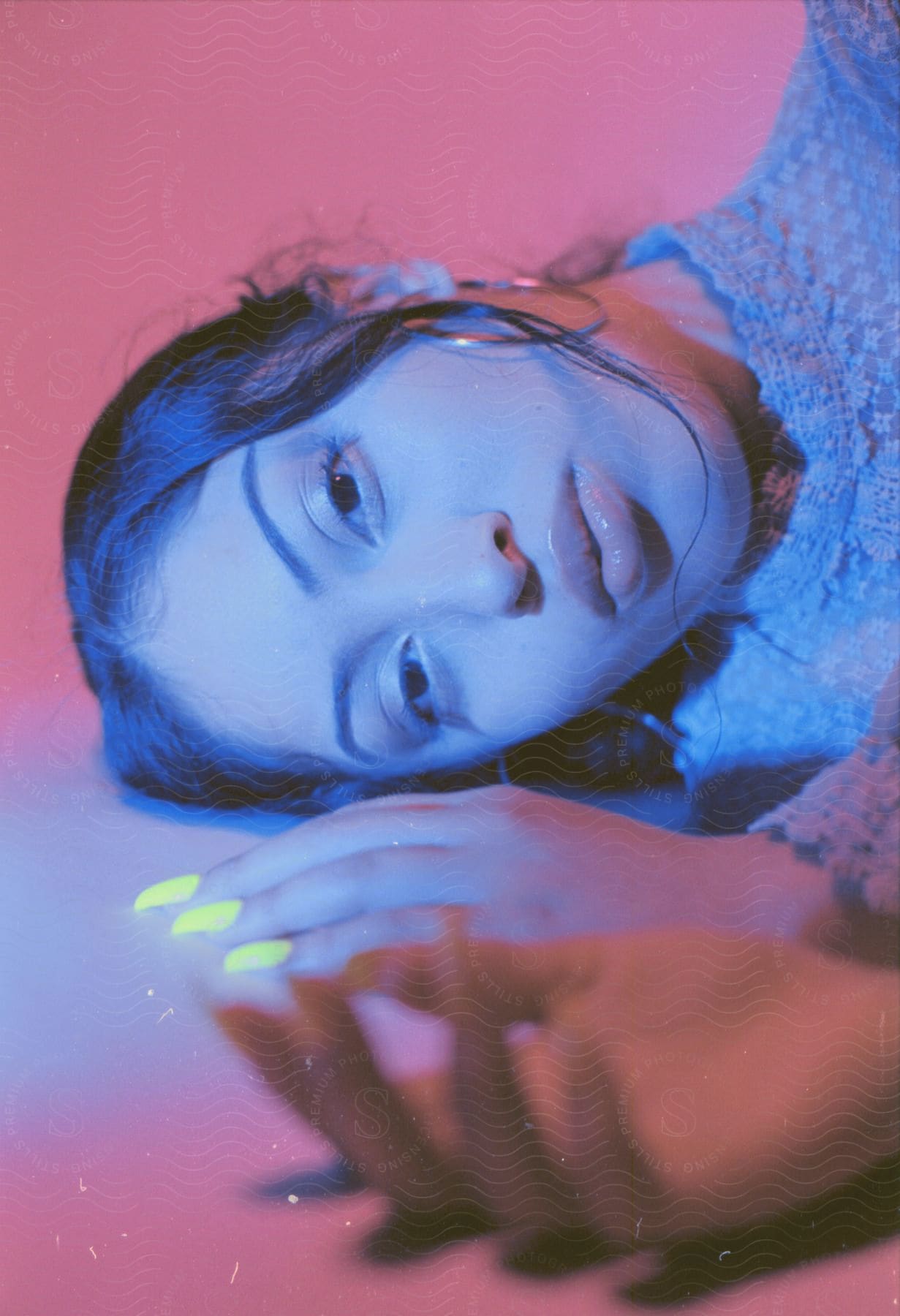 Woman wearing hoop earrings and a blue blouse lies on the ground staring at the camera