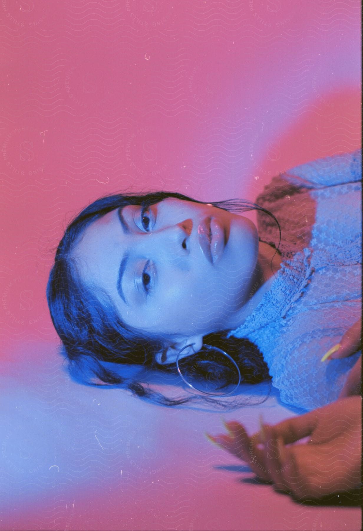 A woman lays on her back while posing for the camera while illuminated with purple light.