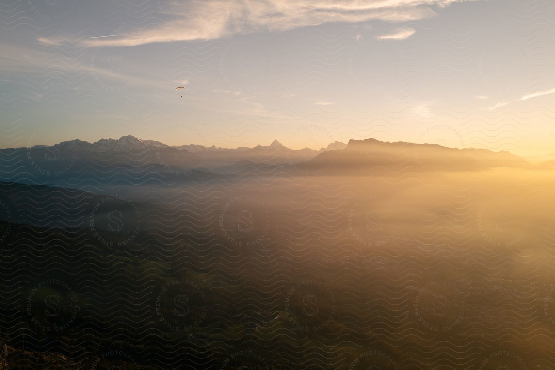 Mountains spread across the horizon under a hazy sky as a paraglider floats across the sky