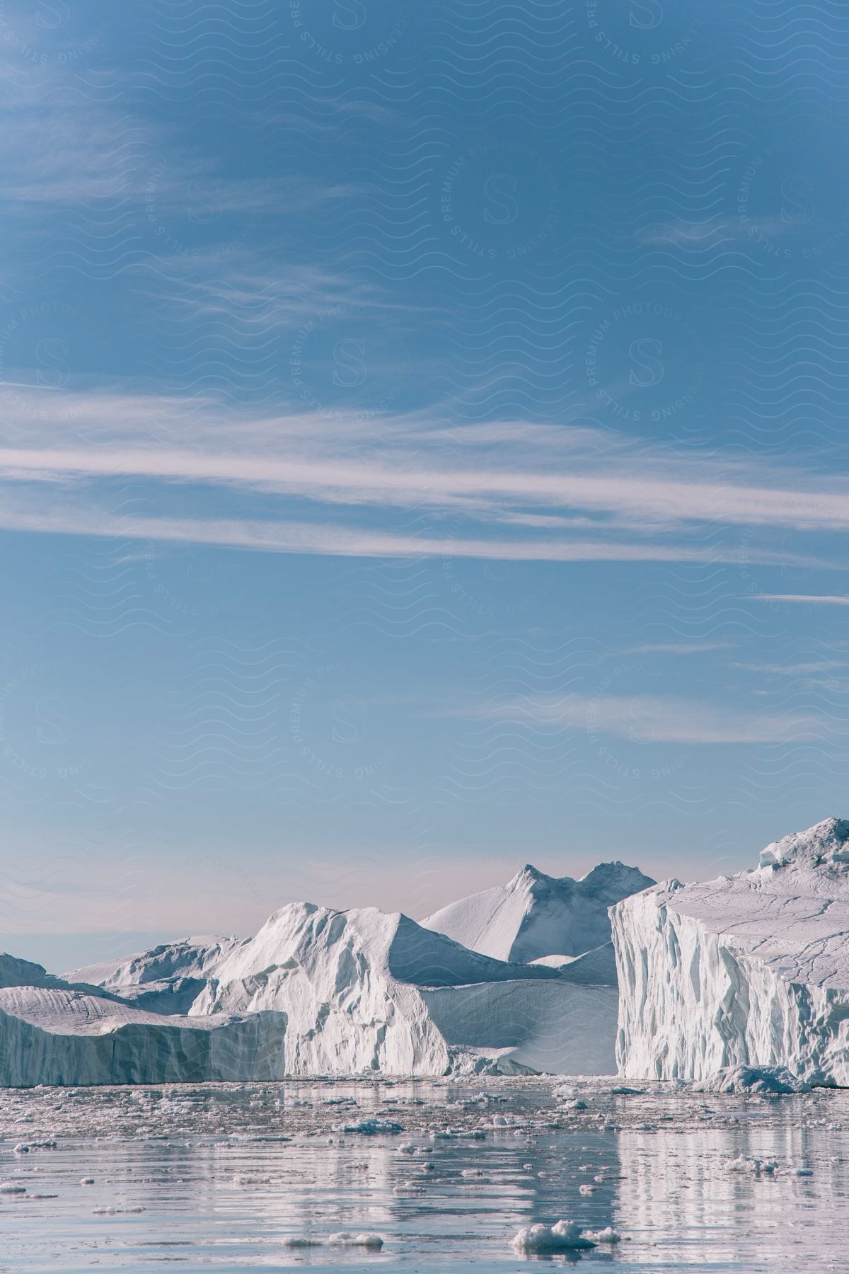 Icebergs and pieces of melting ice float in arctic water under a clear blue sky