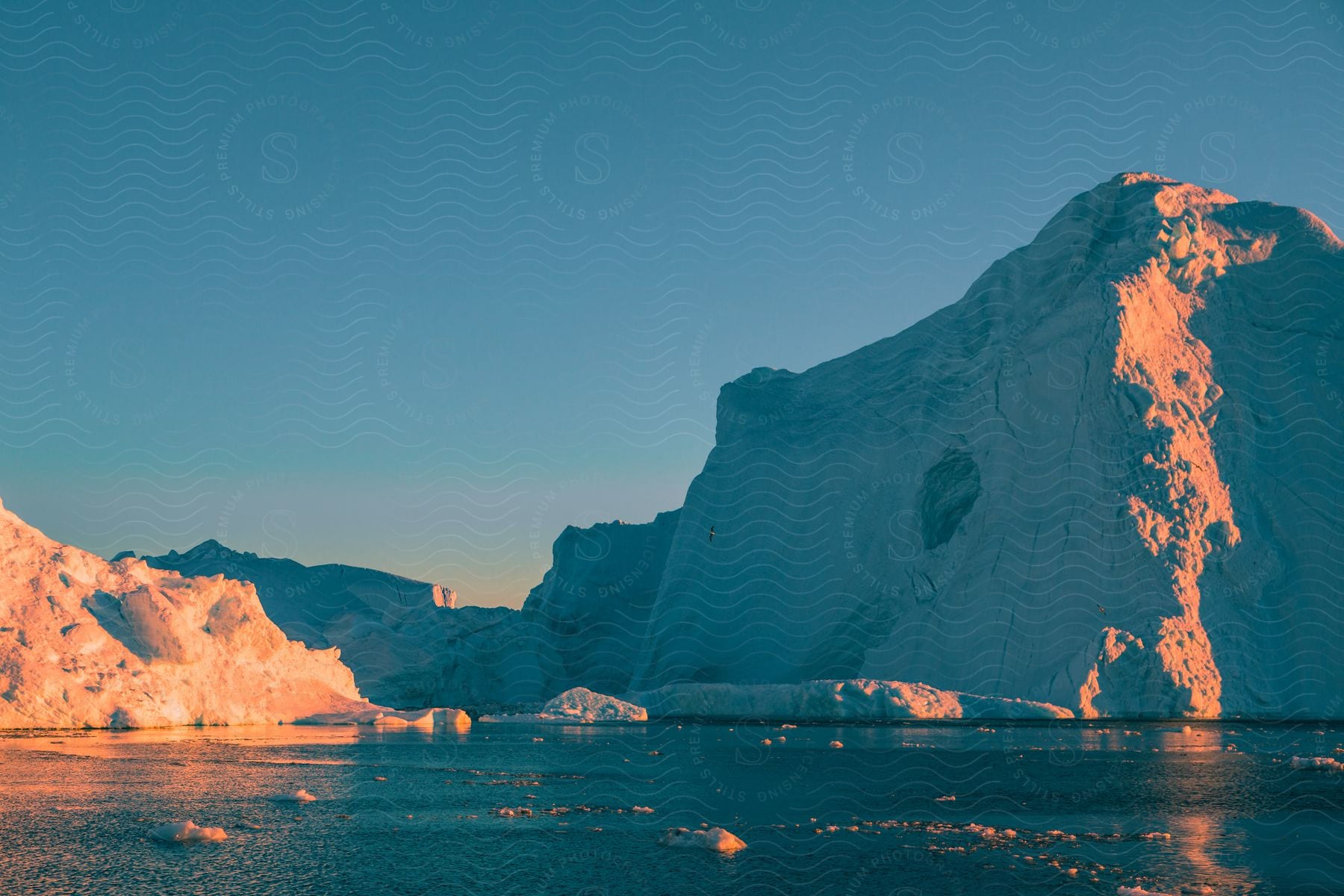 The sun shines on glaciers and pieces of melting ice floating in the arctic water