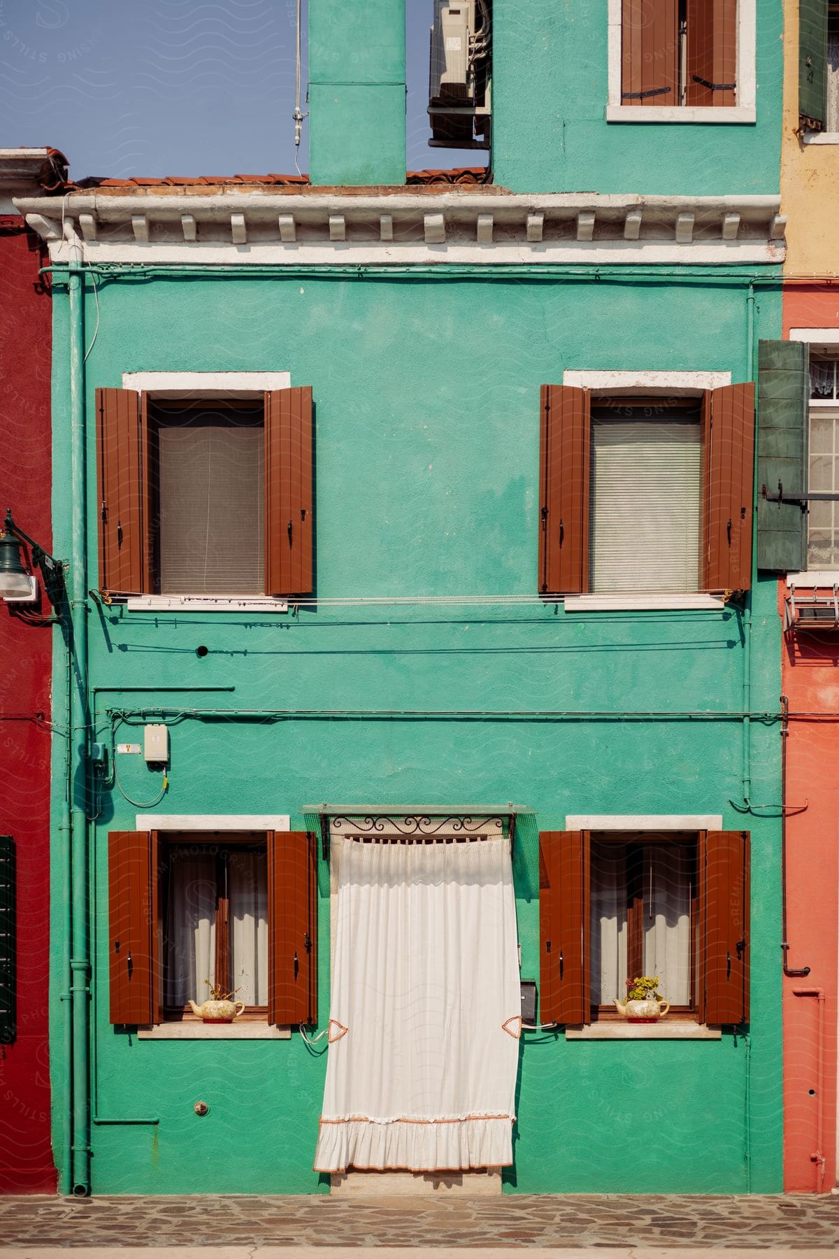 Turquoise building with red window panes and a white curtain for a door in an urban neighborhood