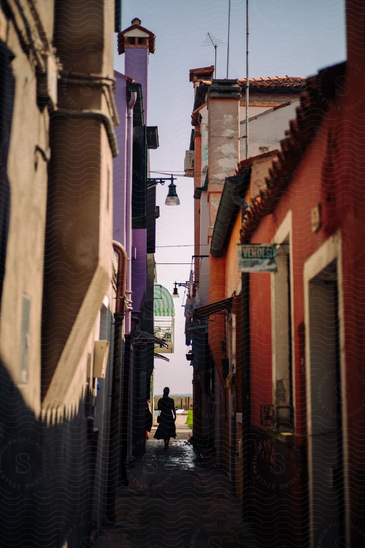 Person walking down a narrow alley way with buildings on both sides creating a shadow effect