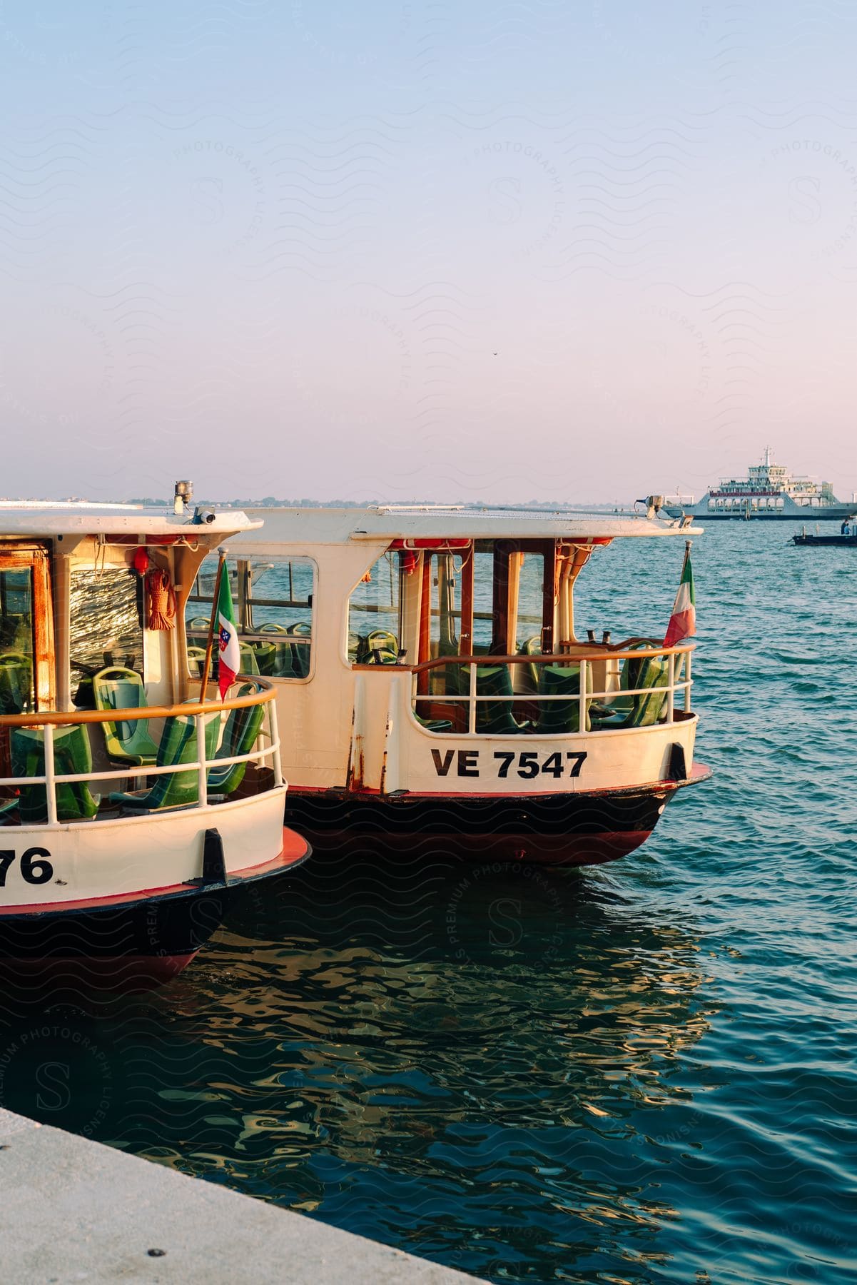 Small ferries docked beside a large ferry on the water with a faded pink and blue sky in the horizon