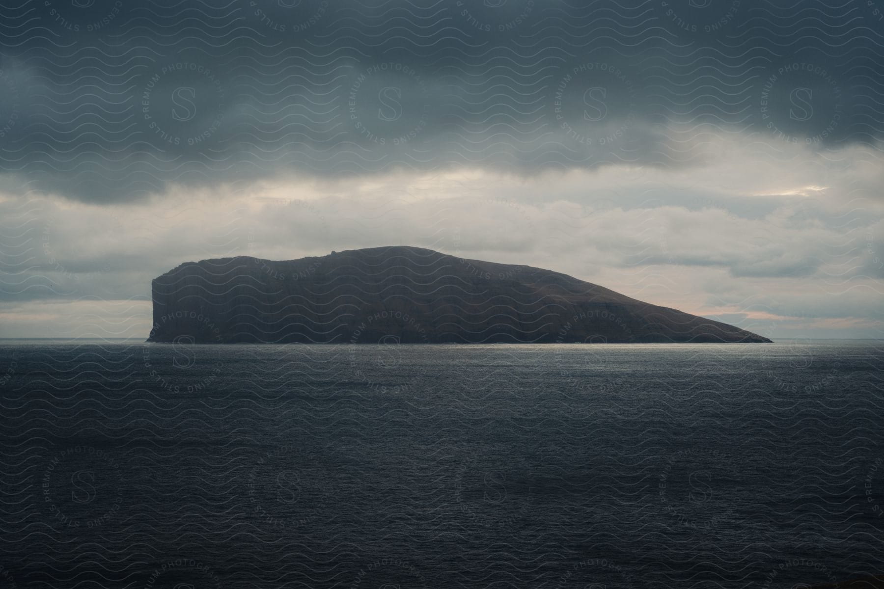 An island with steep cliffs surrounded by calm water and stormy clouds