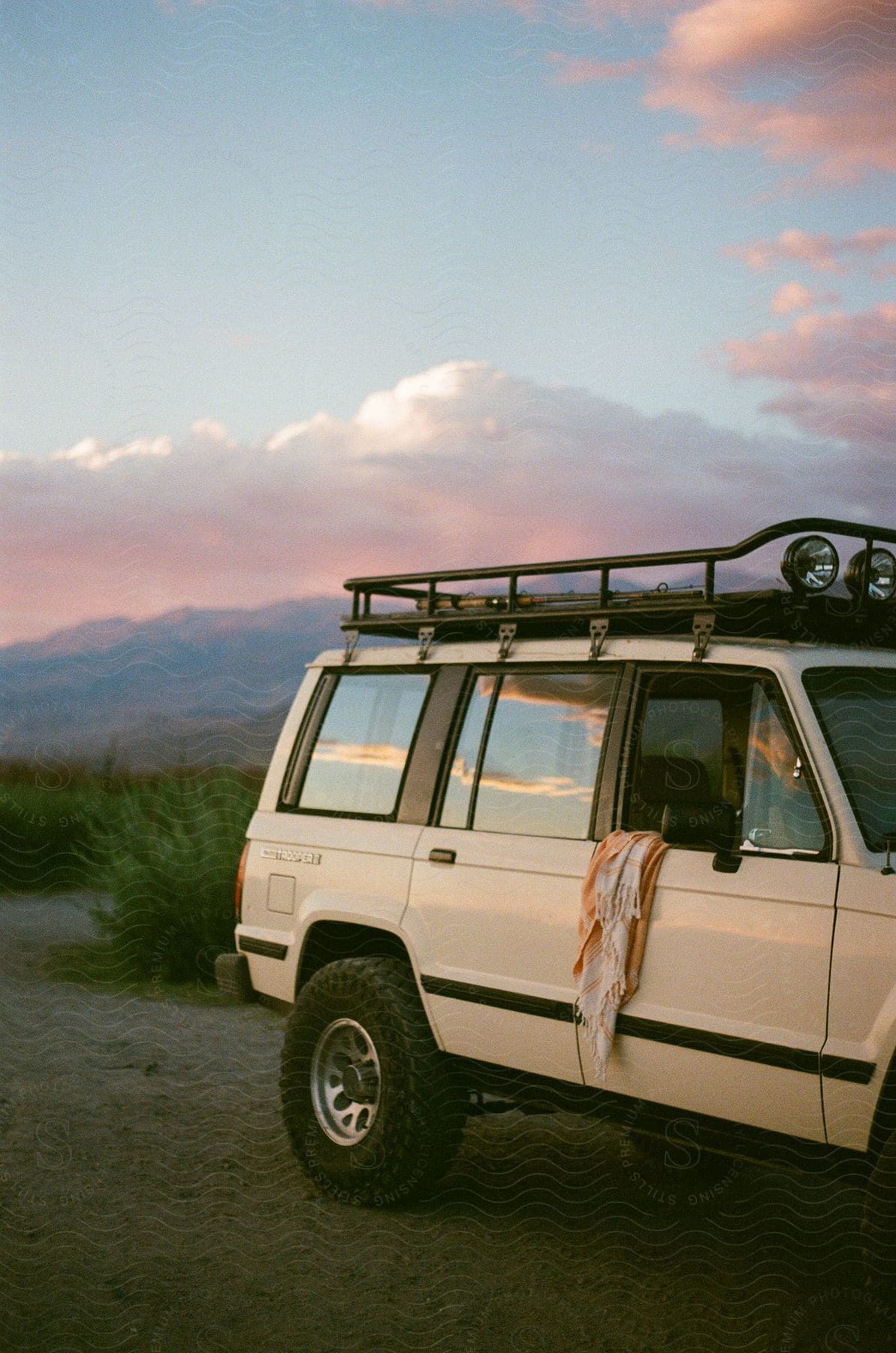 White jeep parked outdoors with the front window down a shirt hanging over it and mountains in the distance