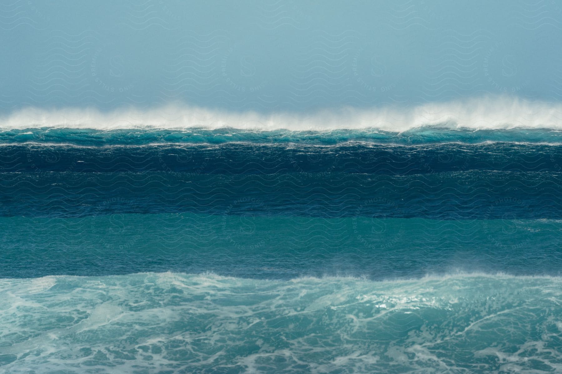 Mist rises from splashing blue water waves as they roll into shore under a clear sky