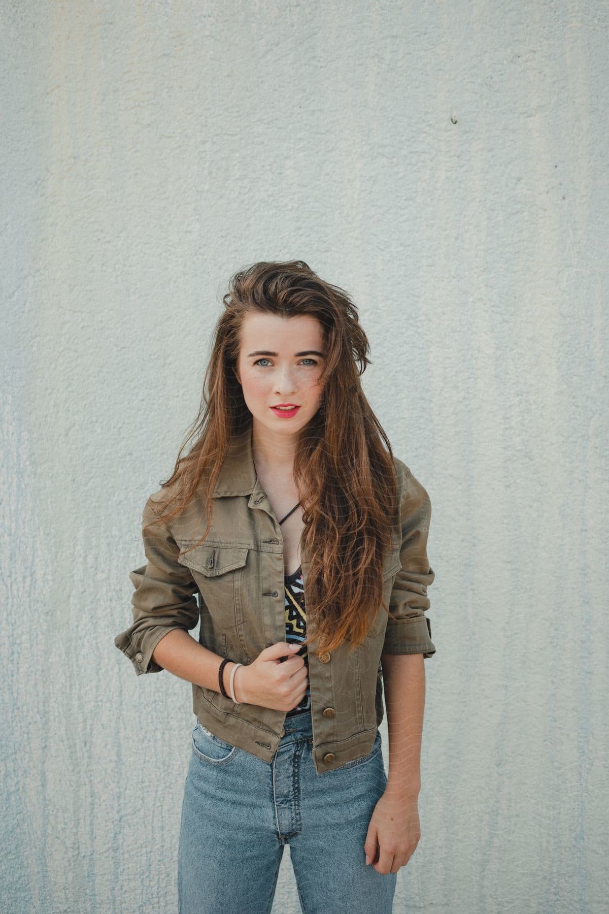 A young woman holds her jacket as she looks into the camera