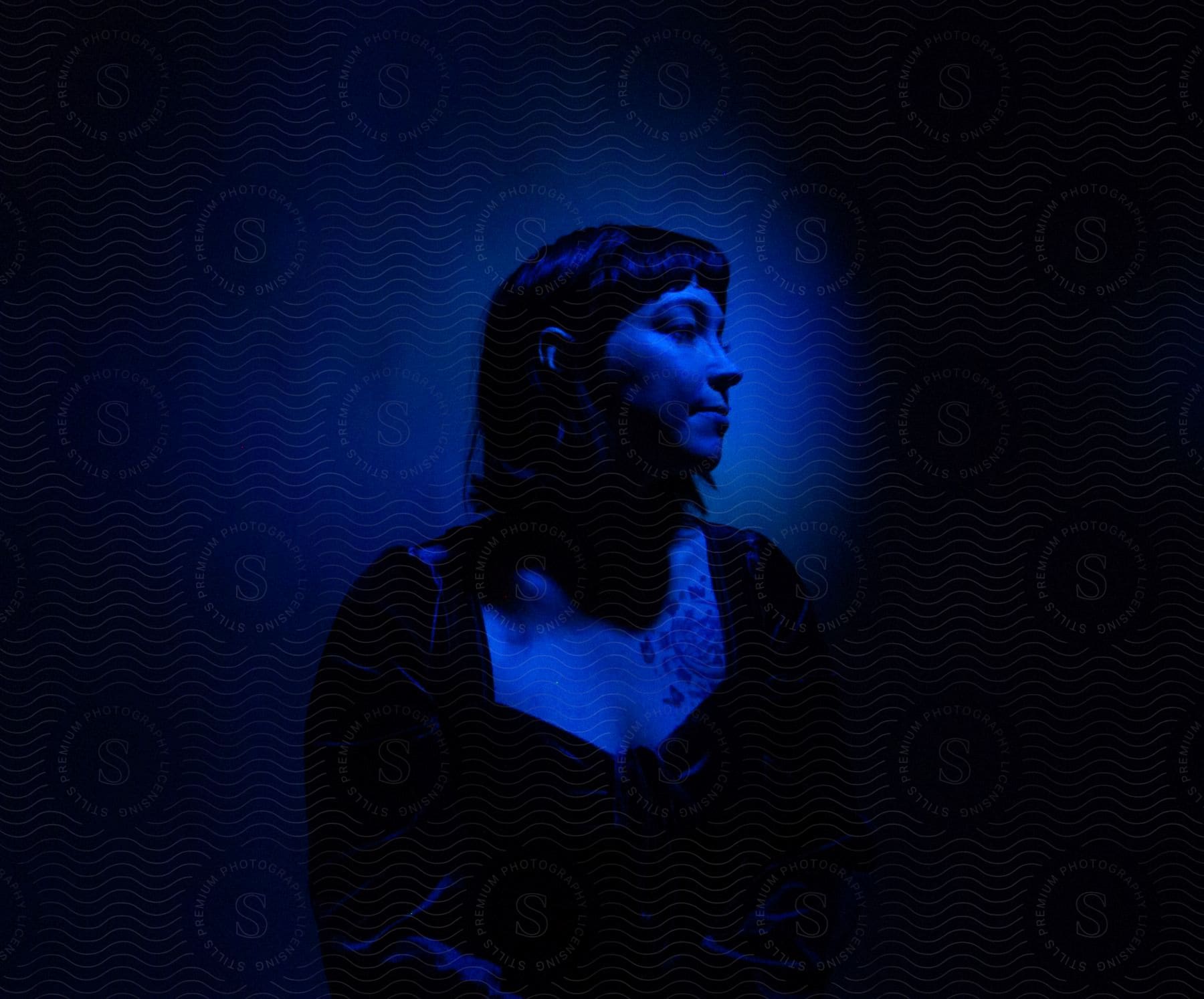 Darkhaired woman wearing dress posing under a dark blue light