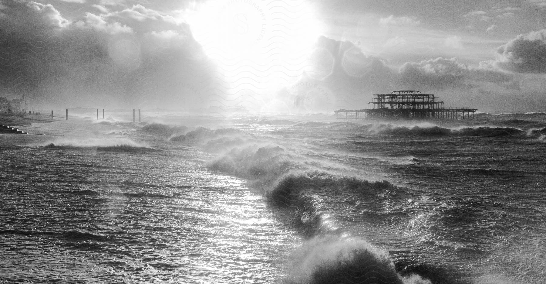 A cloudy day at the beach with a pier structure and rolling waves in the daytime