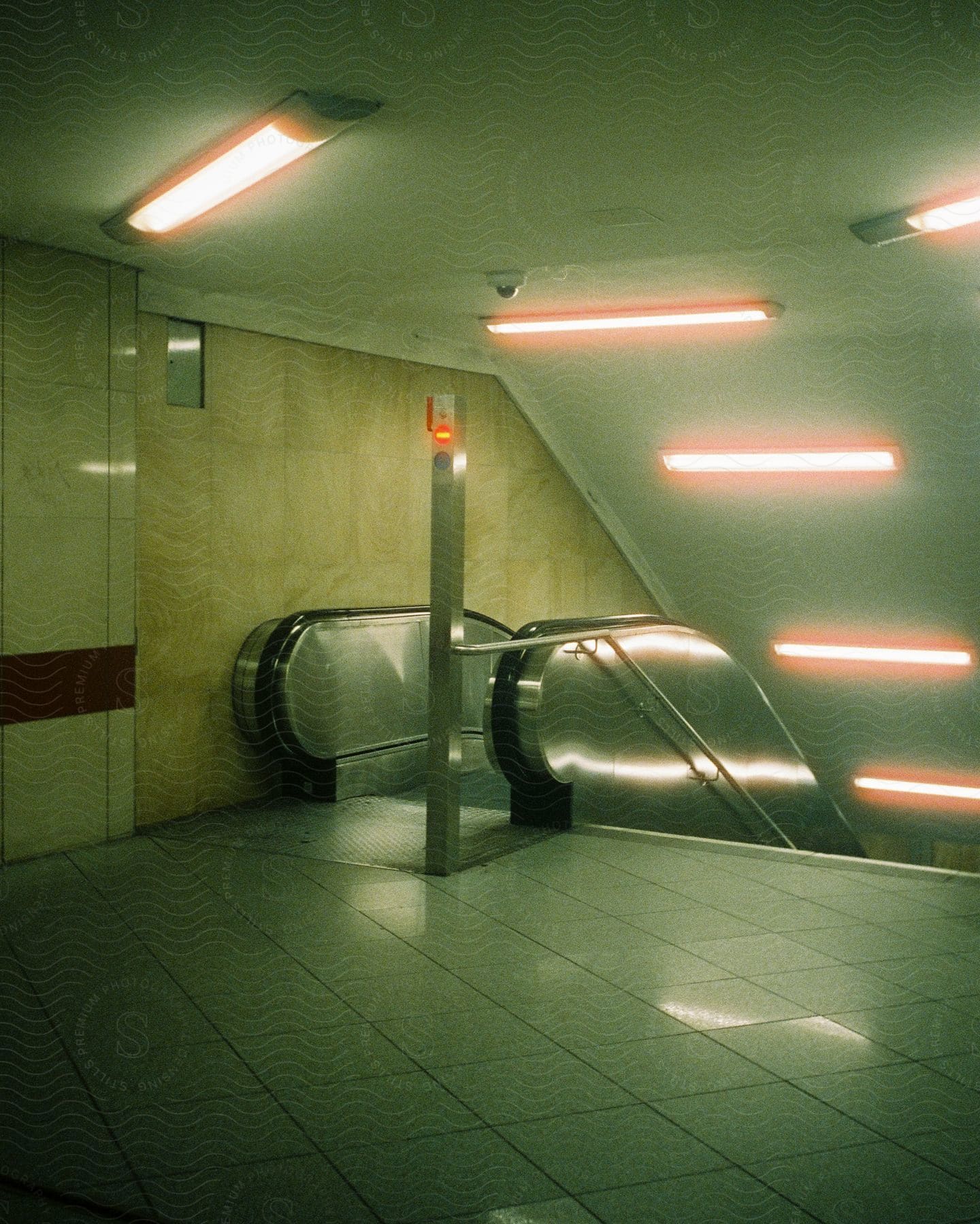 Fluorescent lights glow on the ceiling above the floor and over an escalator in the tunnel inside the subway station of fehrbelliner platz in berlin