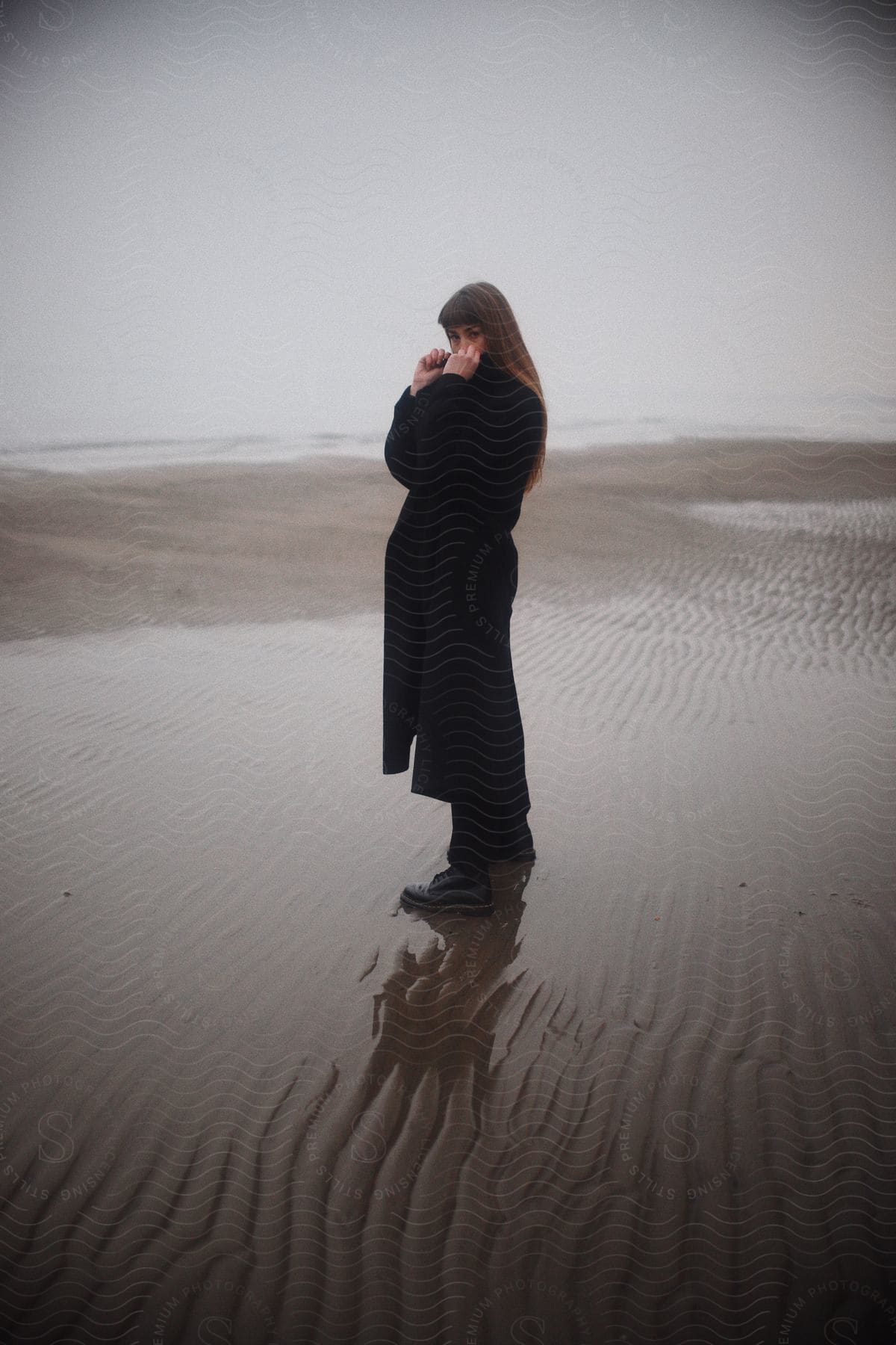 A woman standing on the beach wearing a coat