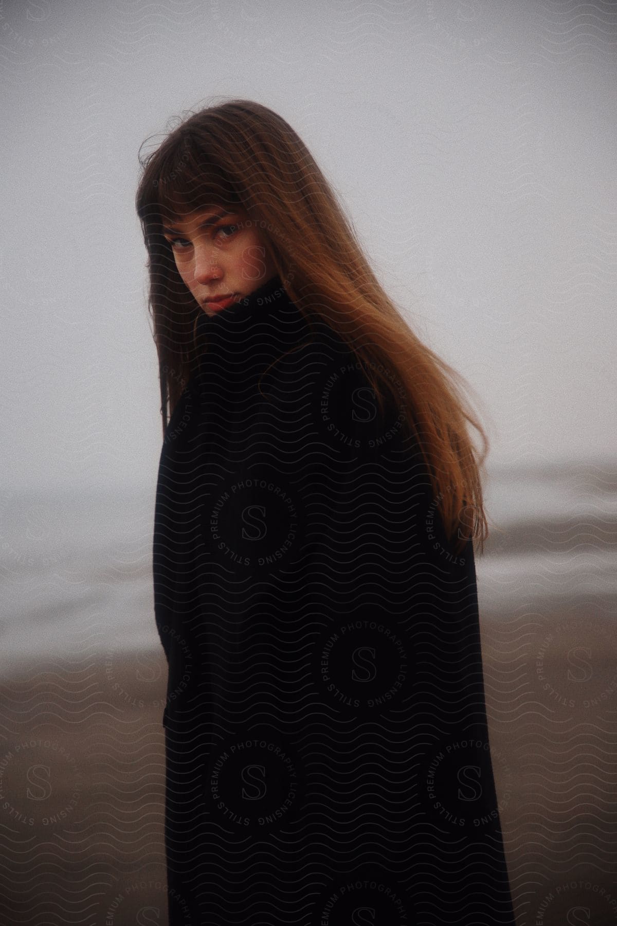 Young woman wearing dark thick coat walking near the coast looking at the camera