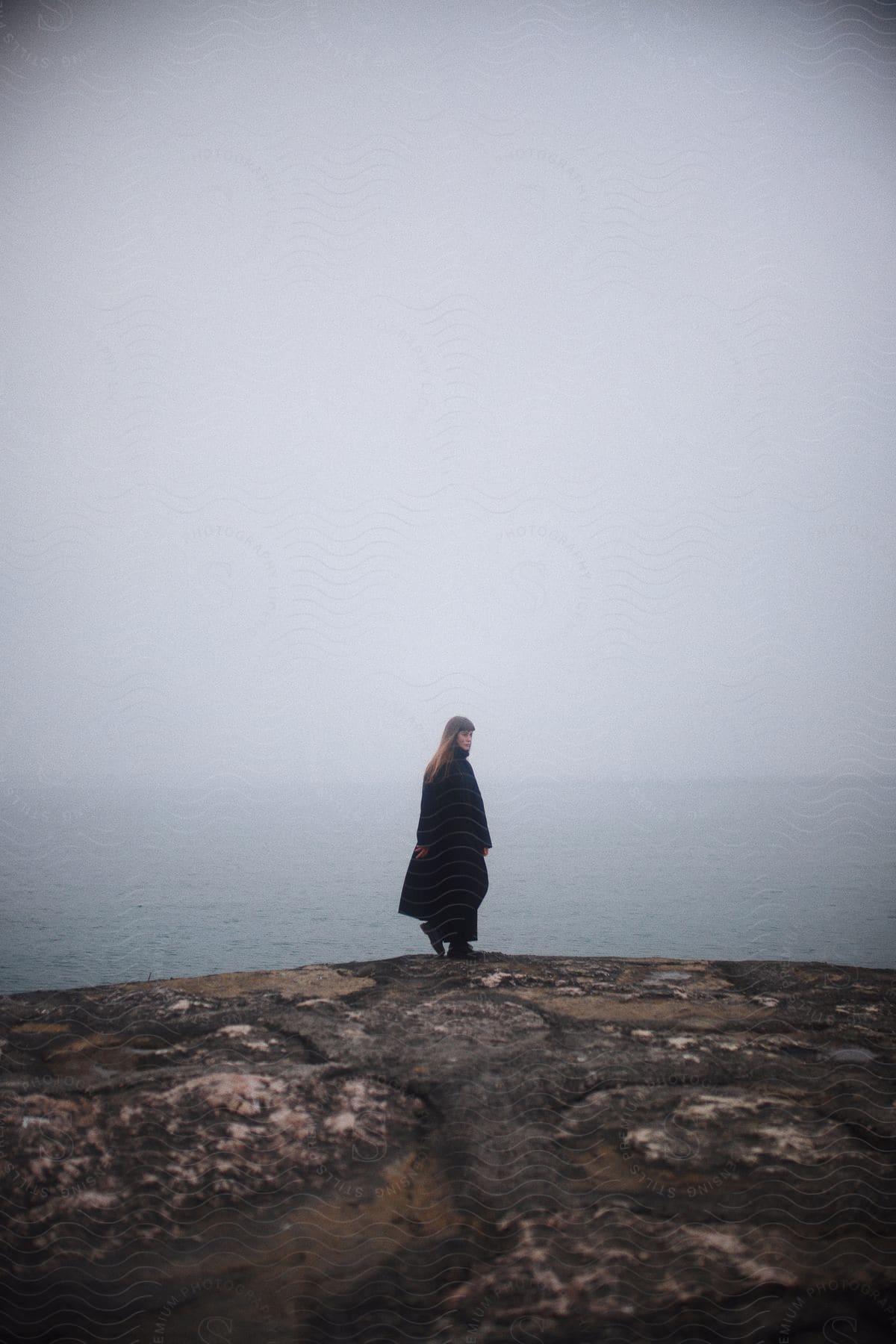 A woman stands on a cliff overlooking the sea