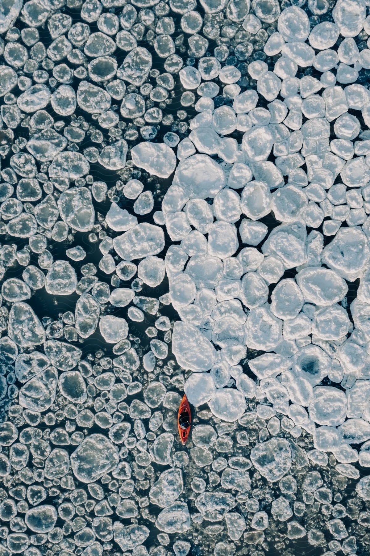 A person paddling a boat through chunks of ice over the water in an aerial shot