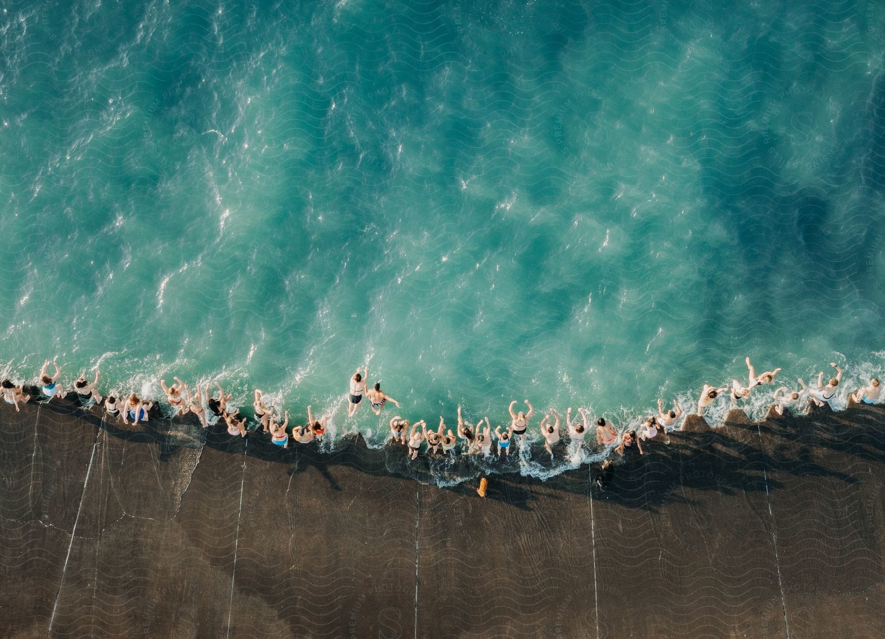 A large crowd of people swimming at the oceans edge where the pier meets the water