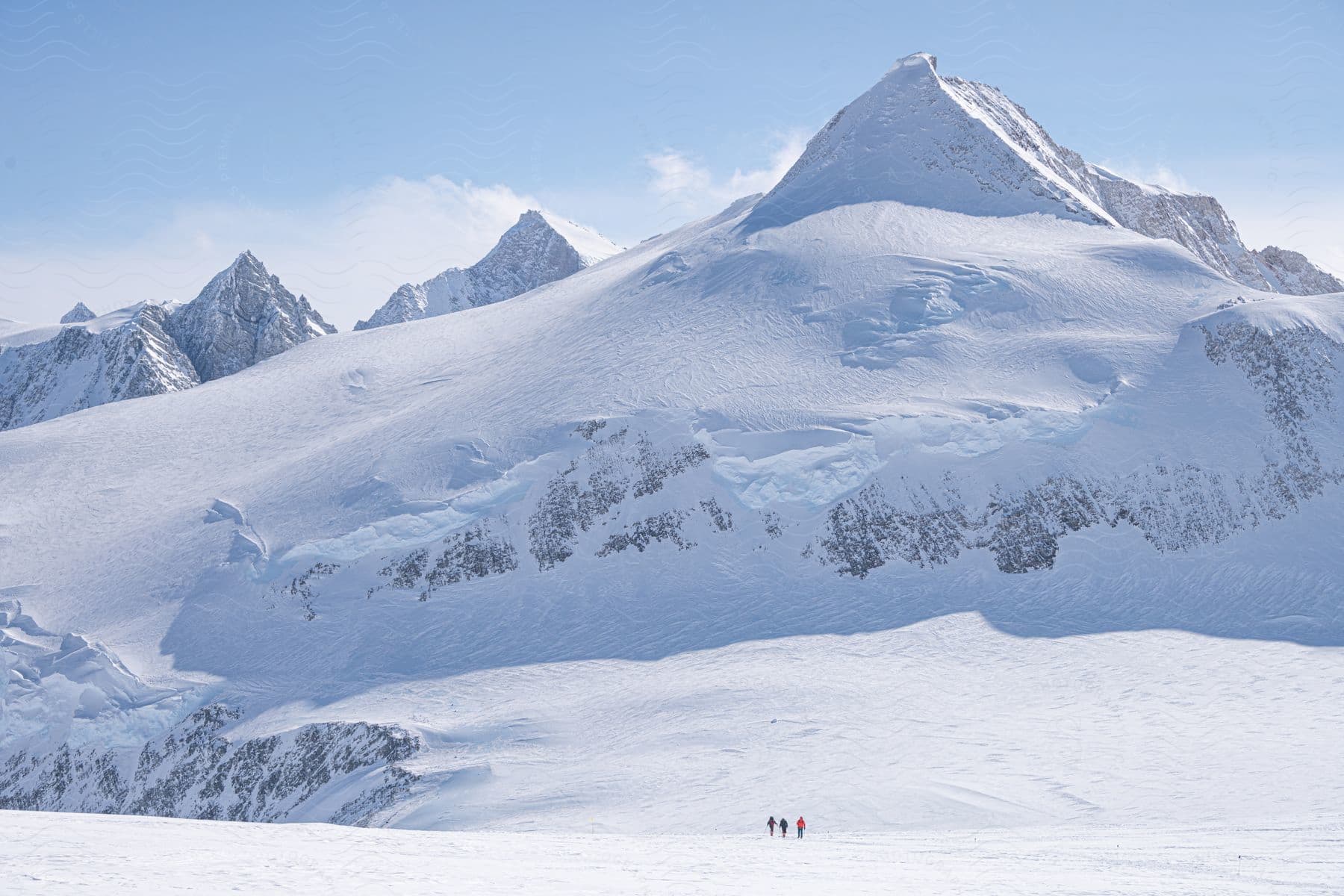 Three adults walking up a large snowcovered mountain in antarctica