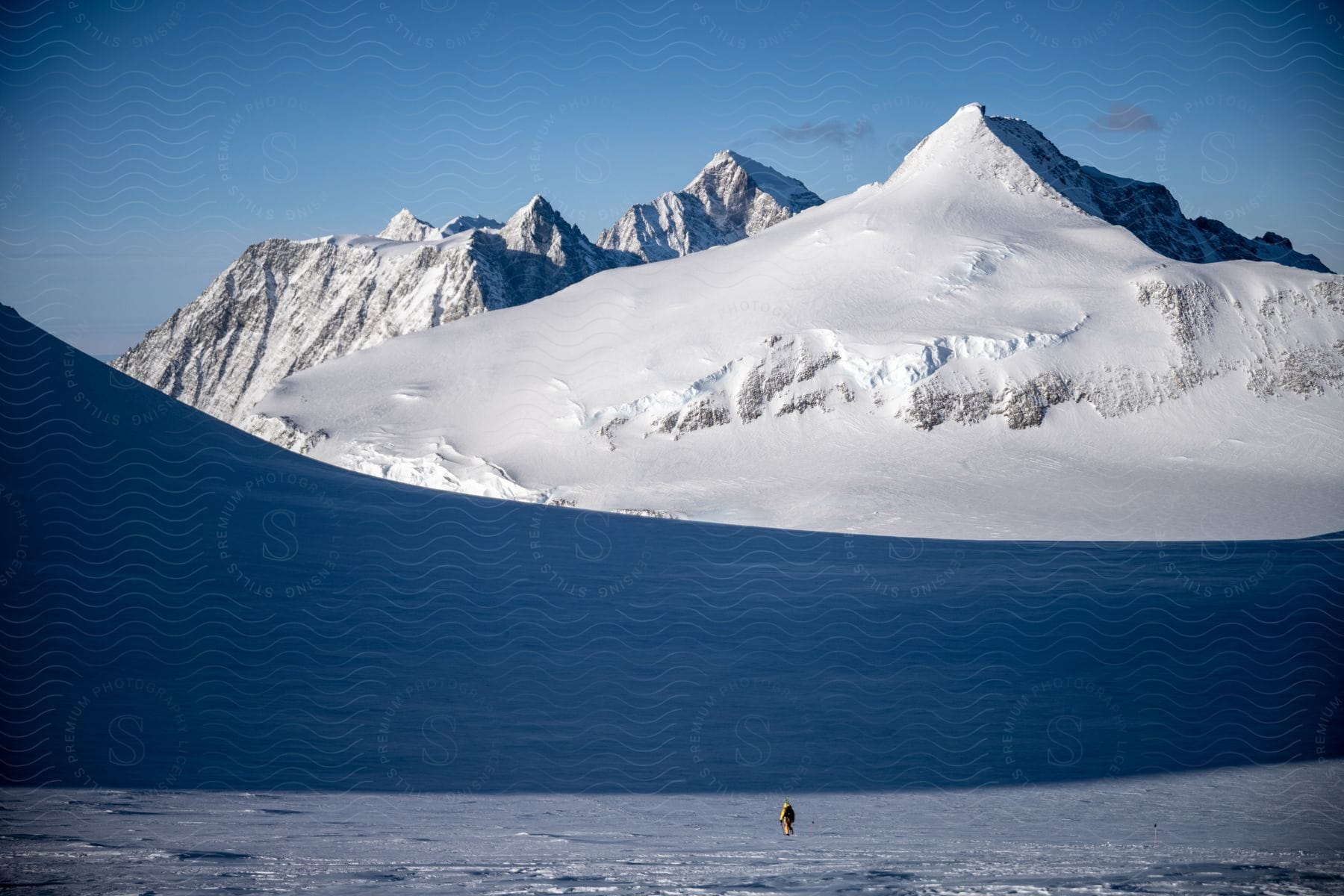 A lone man walking through snowy terrain towards snowcovered mountains