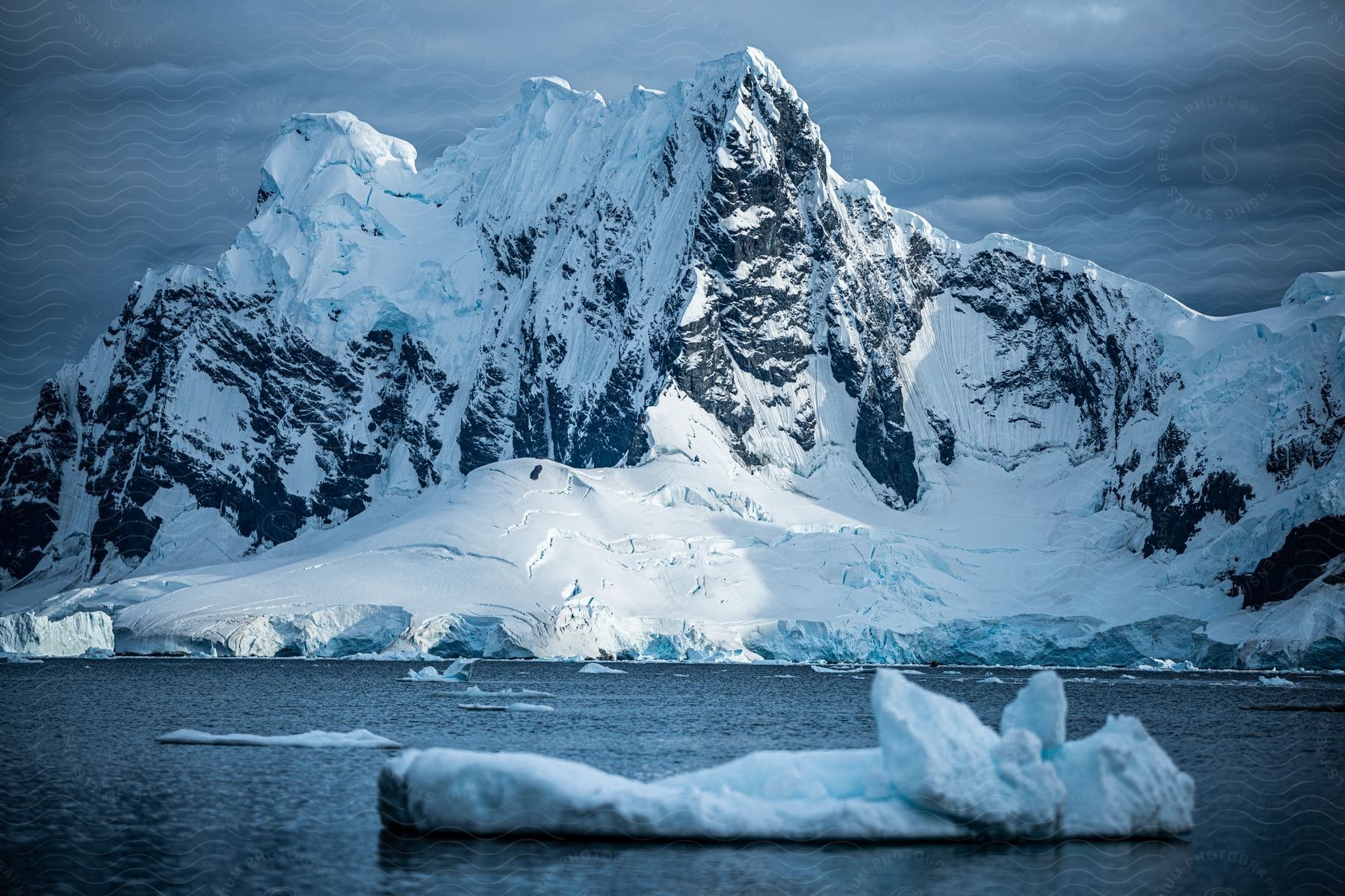 Melting pieces of ice float in arctic water near a glacier under a cloudy sky