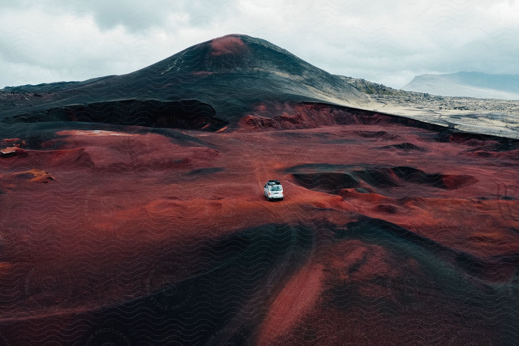 A white van travels on an open road toward a mountain under a cloudy sky