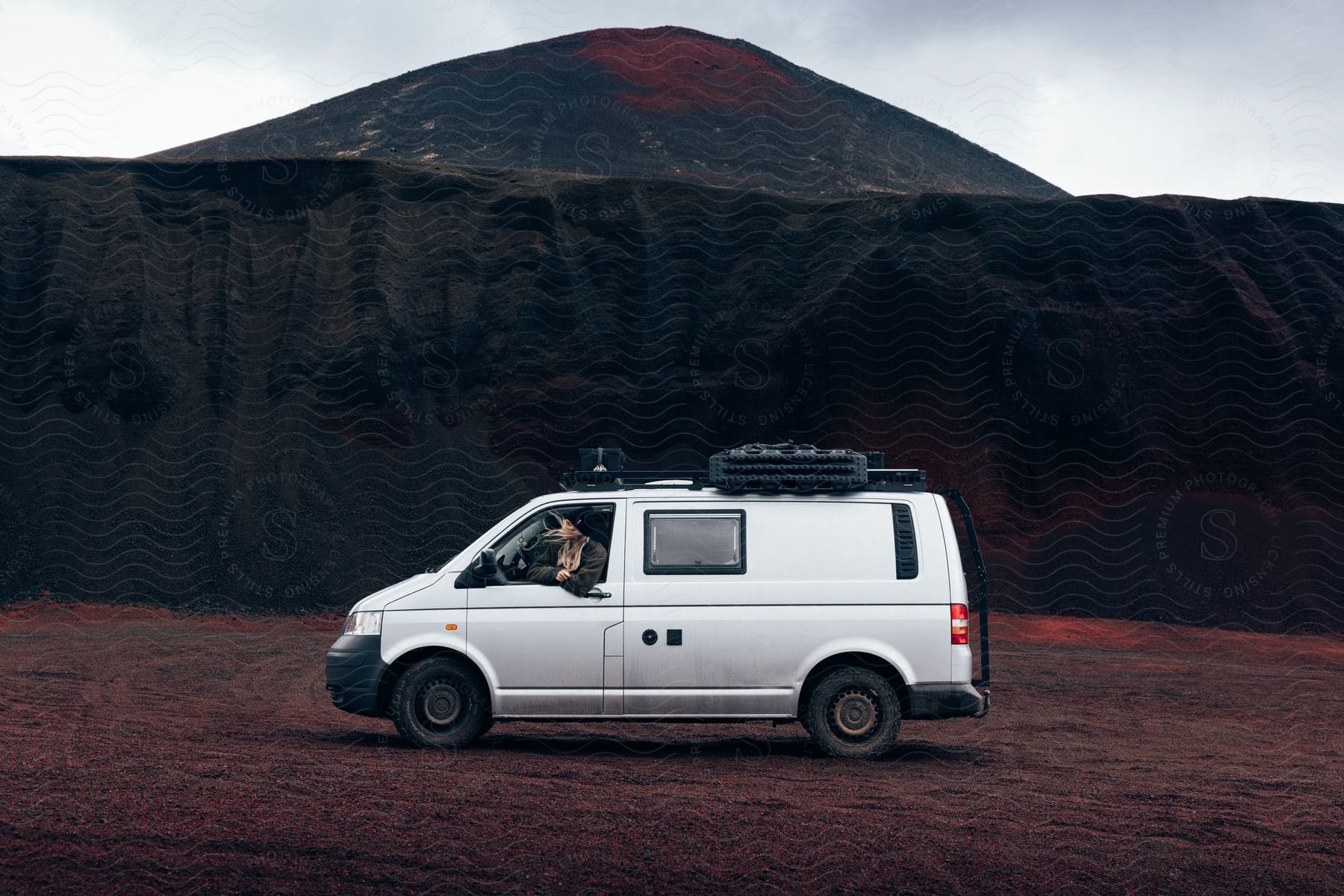 A lady sitting in a bus surrounded by dry land and hills