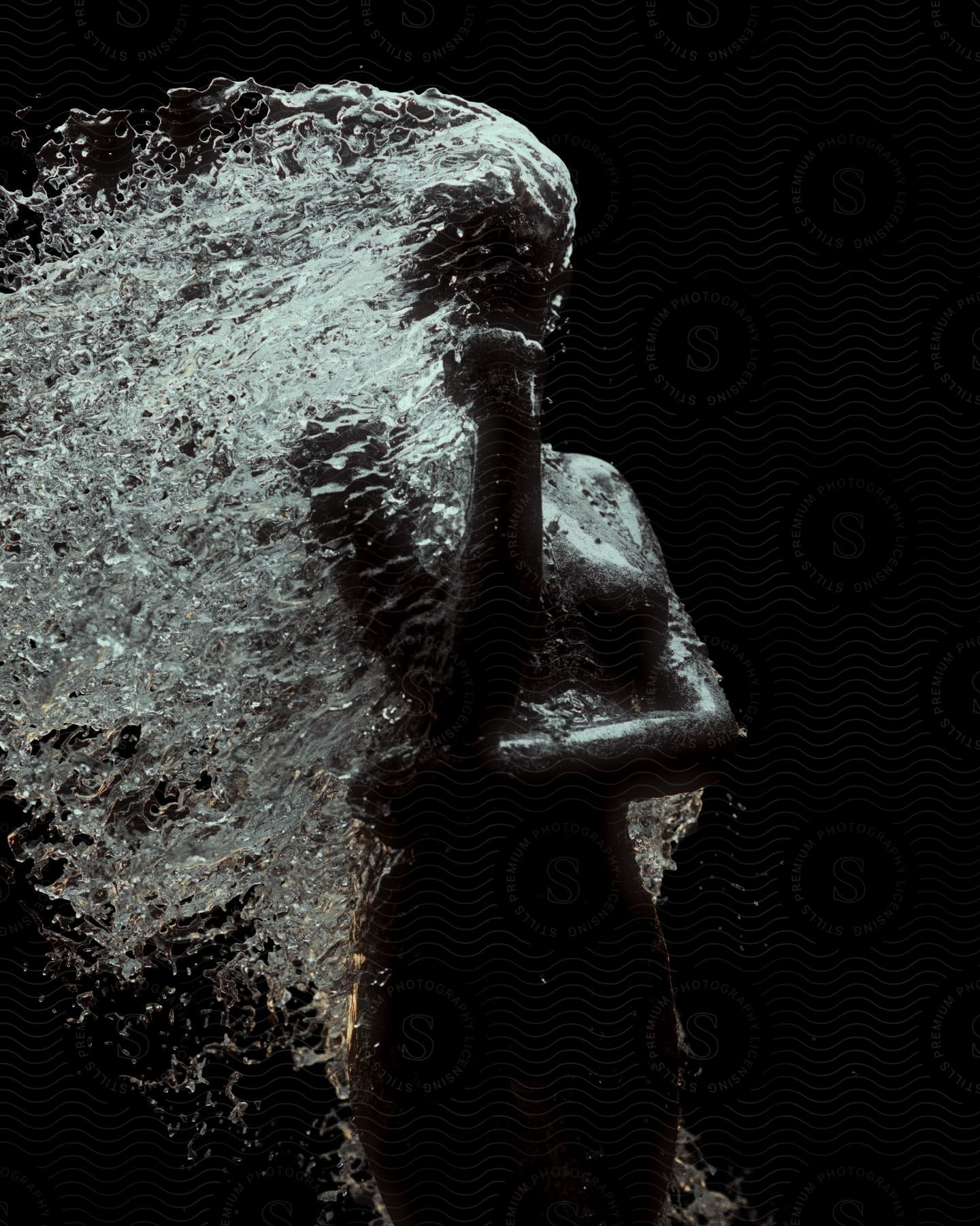 Black statue of a woman with water splashing over the sculpture against a black background