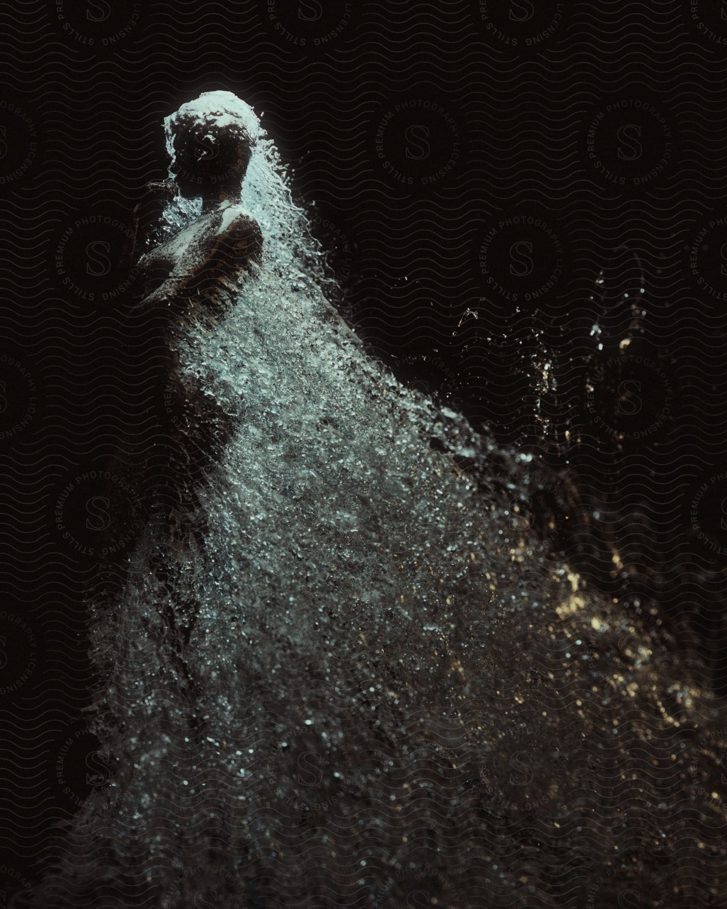 A person posing nude with water splashing off of them on a black background indoors