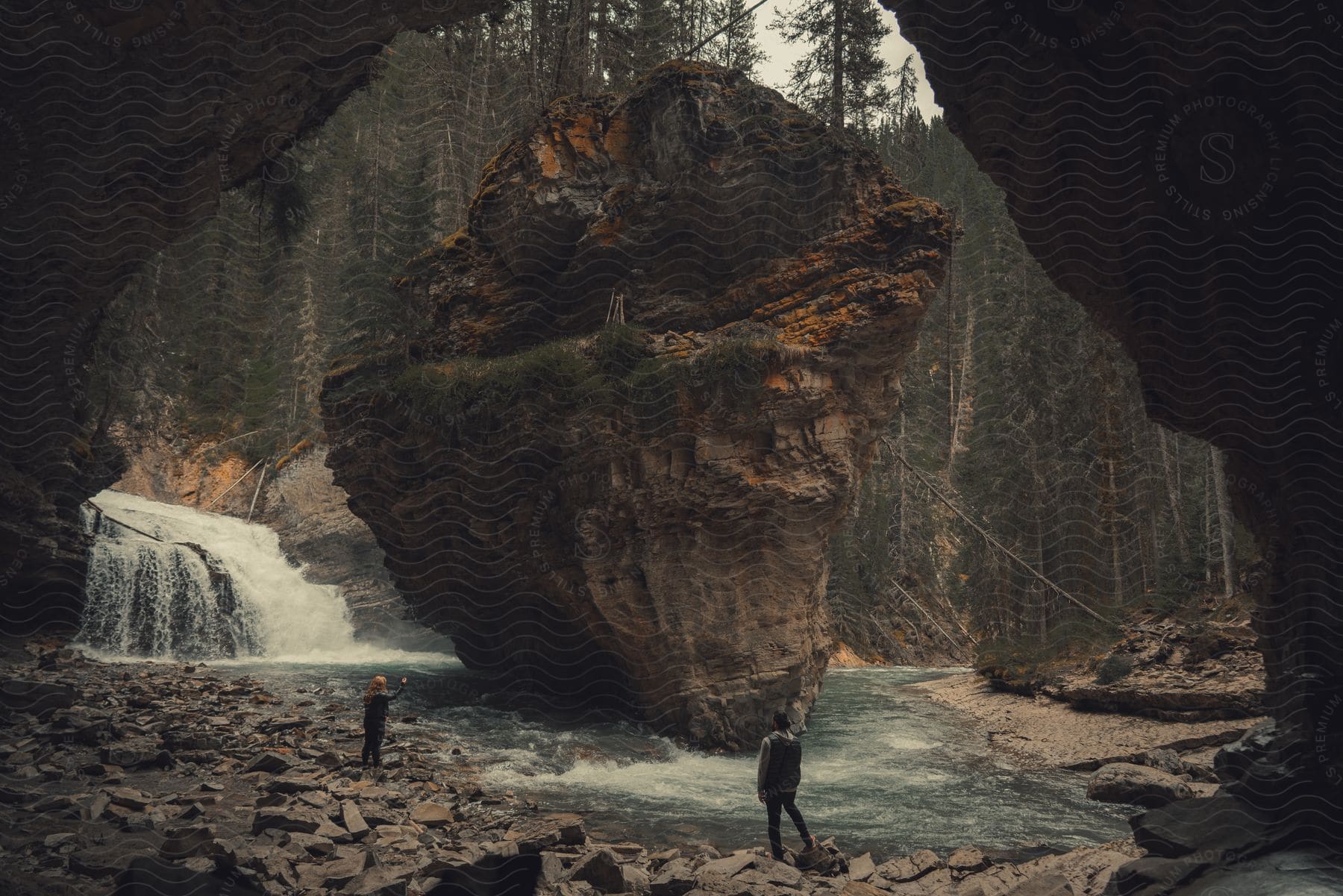 Two people standing near a rocky cave by the water in the rockies during summer