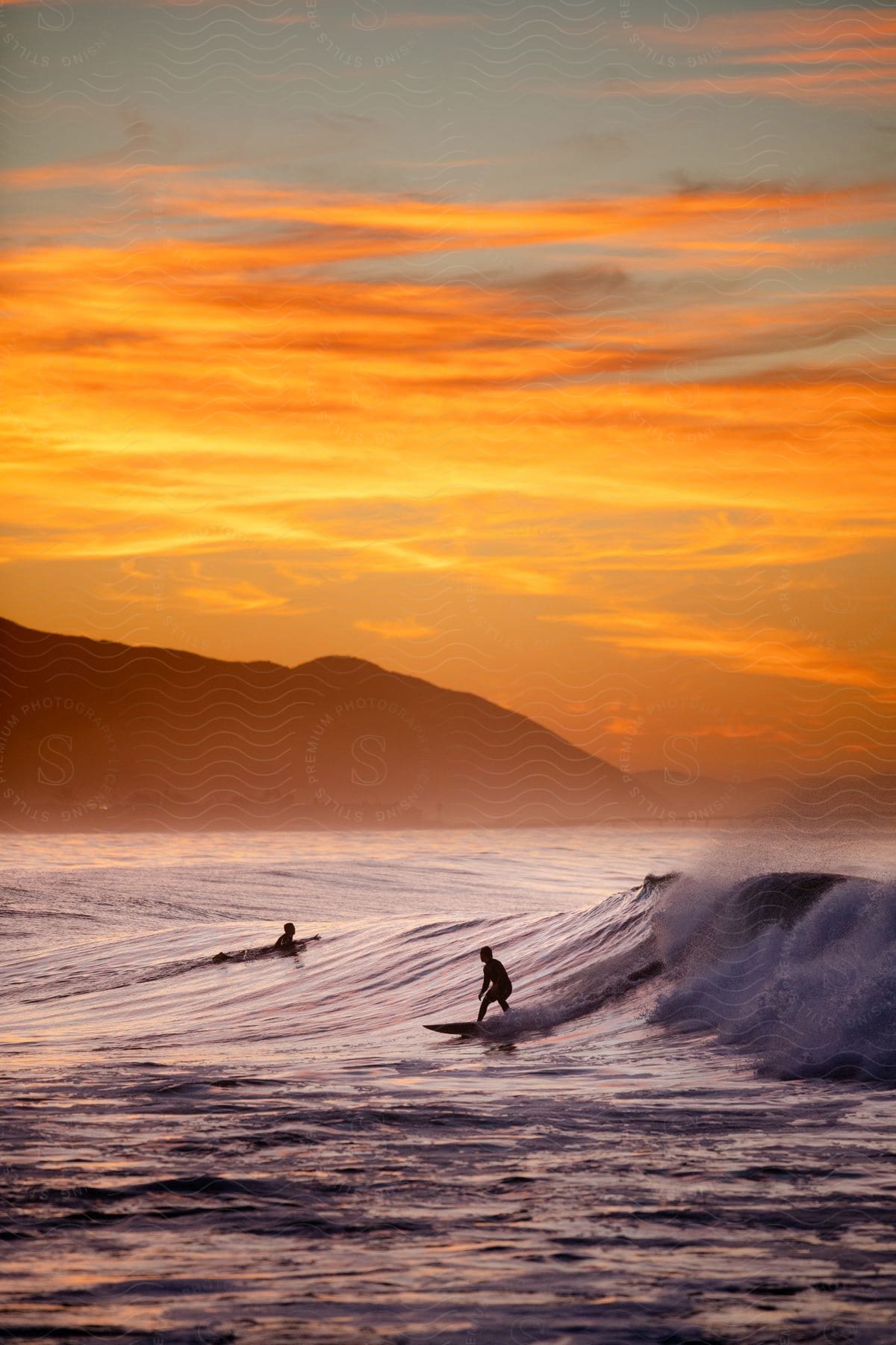 Two surfers one riding a wave and the other paddling to the top at sunset on the central coast of california
