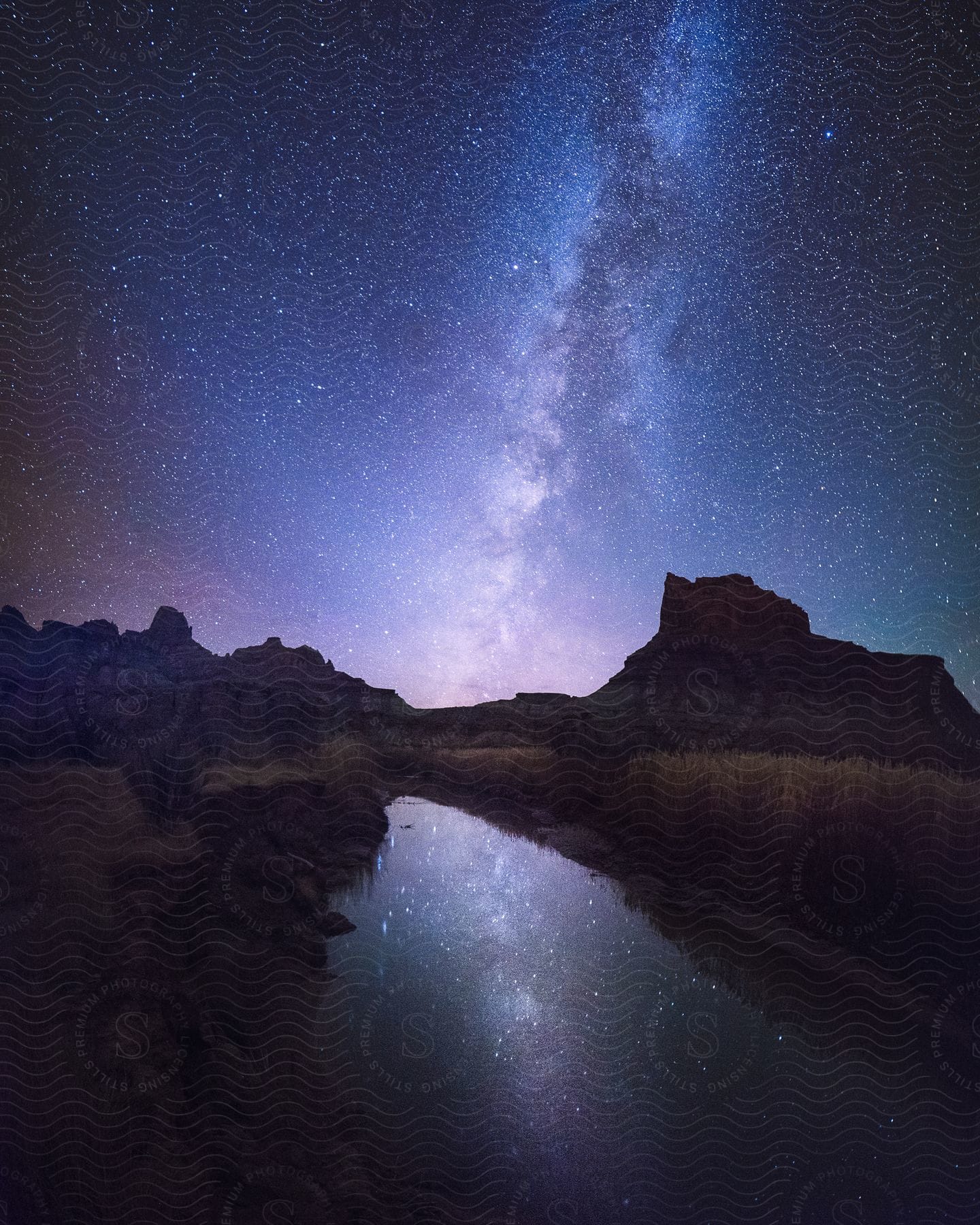 A tranquil night sky with stars and a nebula over a rocky landscape