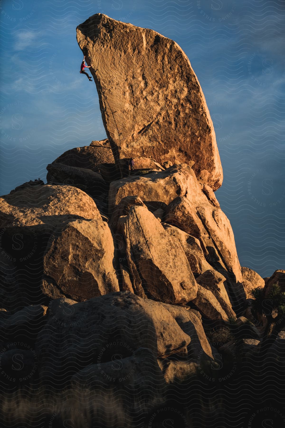 A mountain climber holds on to the side of a rock formation high in the air in joshua tree national park