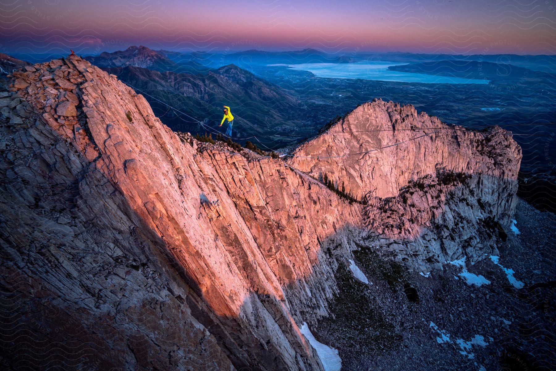 A hiker climbs a steep peak with a serene sunset and calm lake in the background