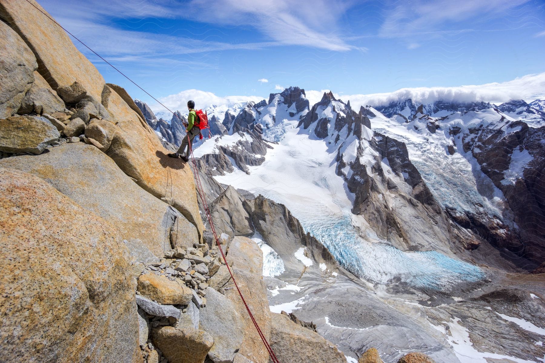 Mountain climber stands on mountainside overlooking ice and snow topped mountain holding rope