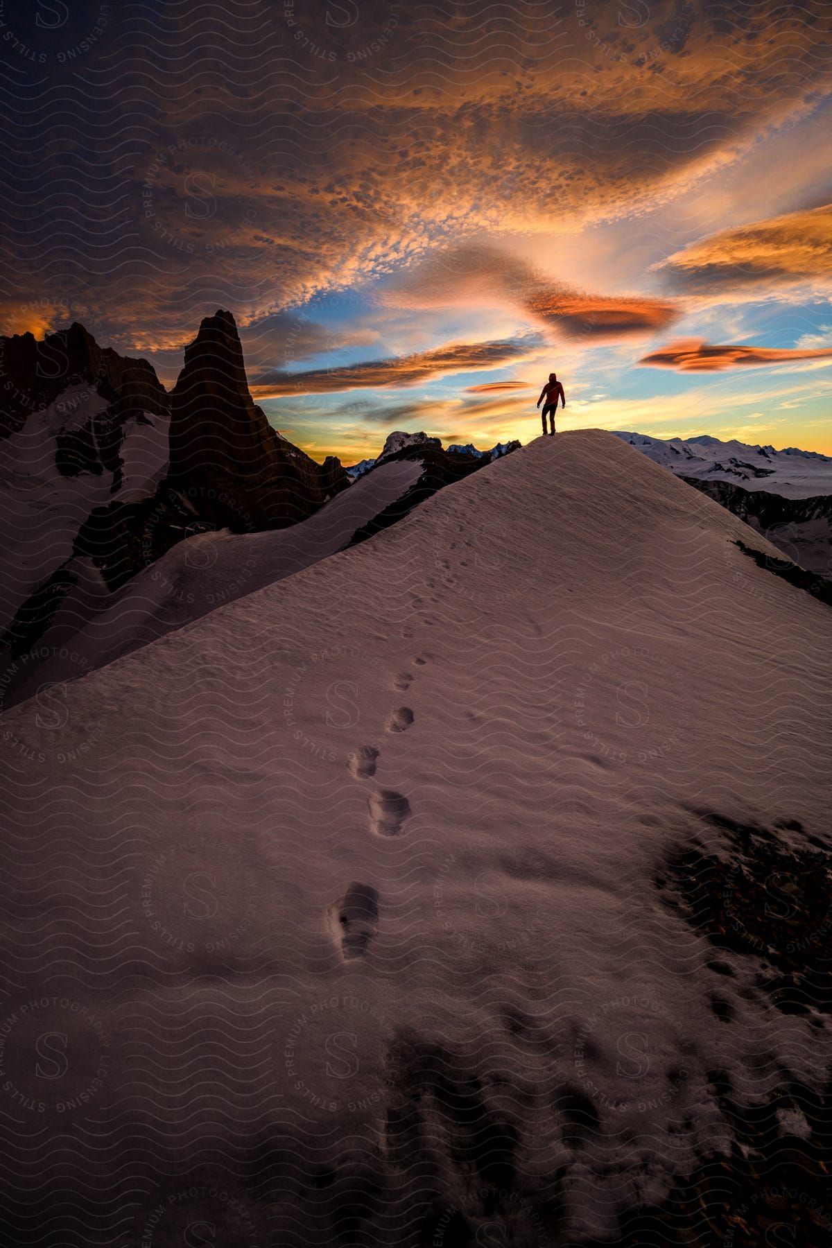 Snowy mountain landscape at dusk with a person at the top and footprints in the snow
