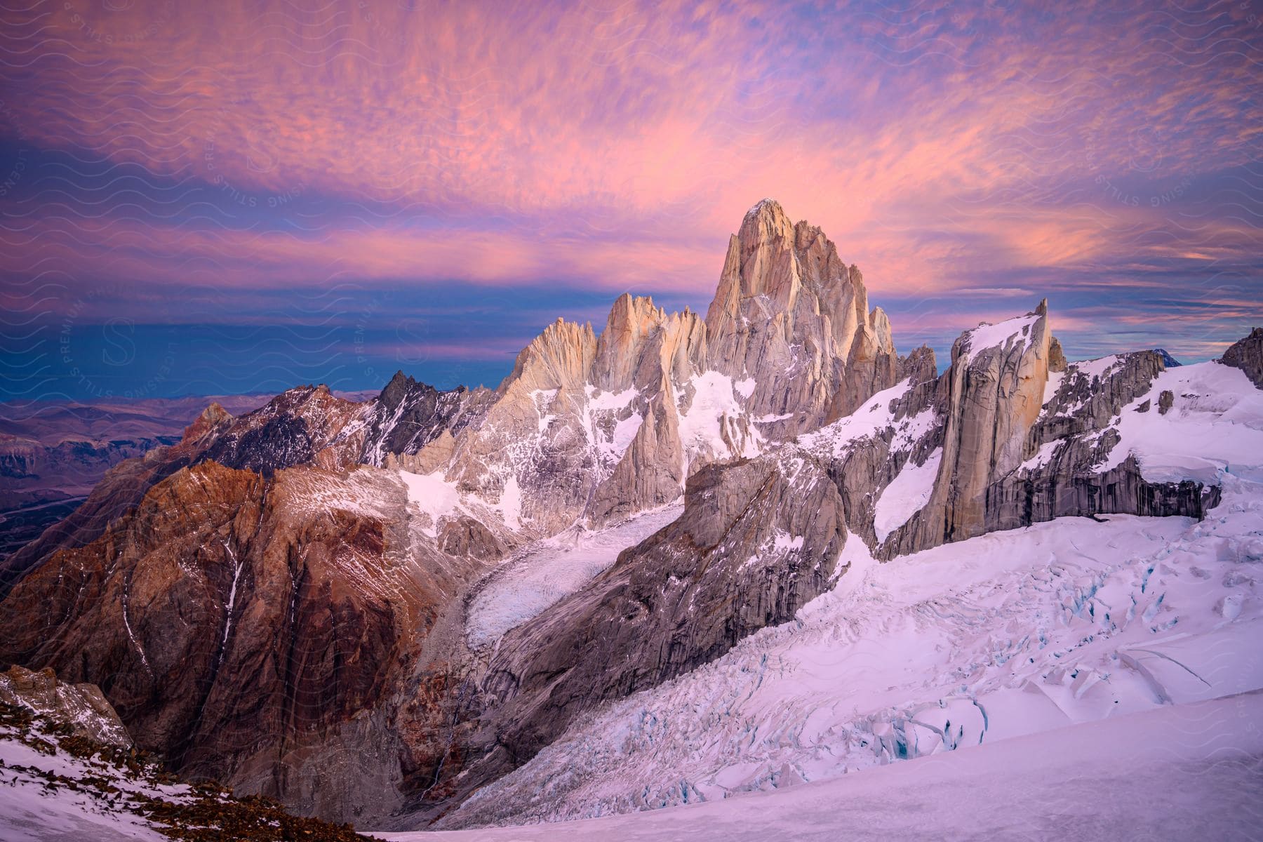 Orange light illuminates a snowy mountain range under a cloudy sky in el chalten patagonia