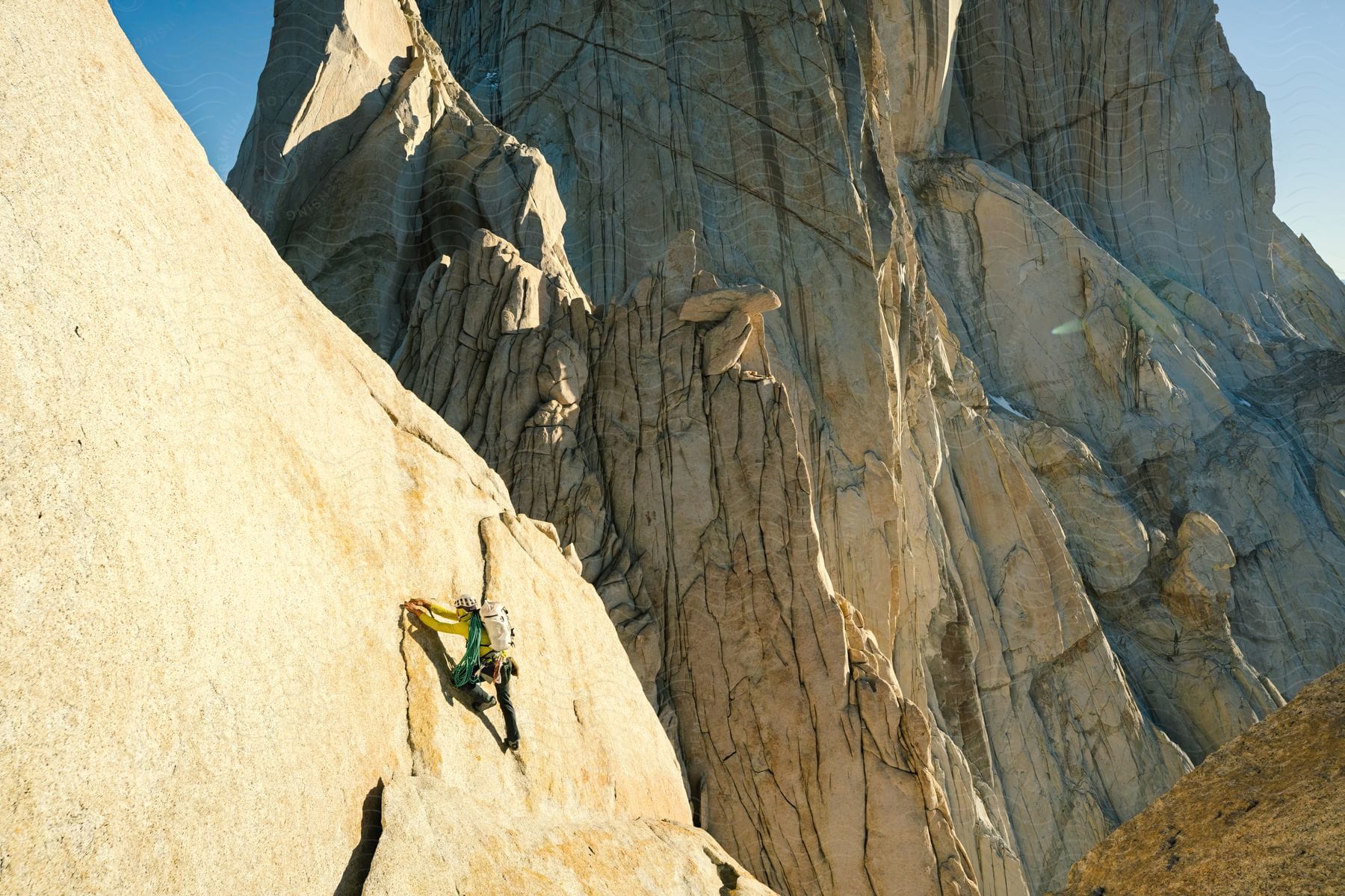 Rock climber prepares for next move on steep mountainside with another tall mountain behind