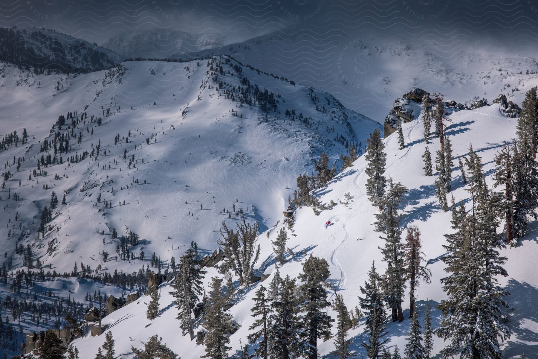 Snowcovered mountains with trees spread across under a cloudy sky