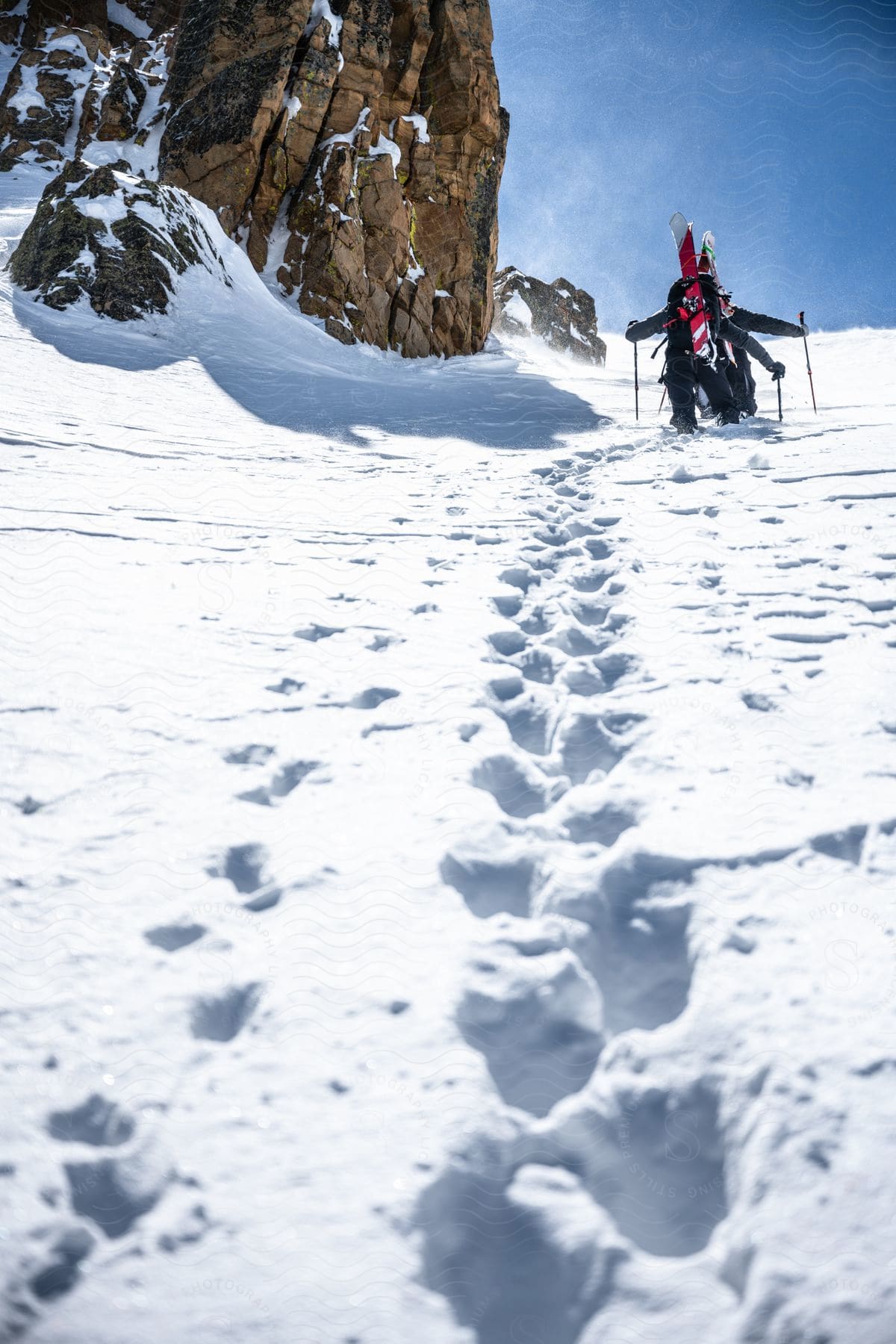 People with snowboards walking down a snow covered path on a mountain on a bright winter day