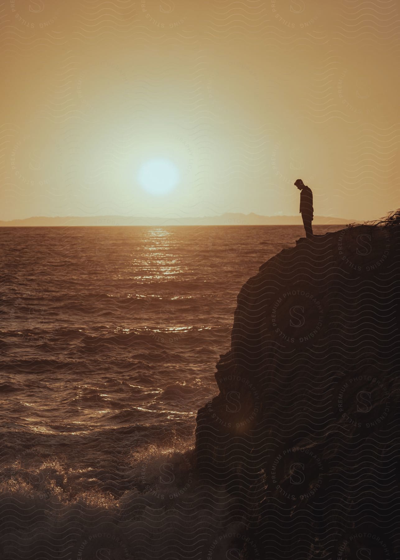 A man stands on a cliff overlooking violent waves crashing onto the shore below