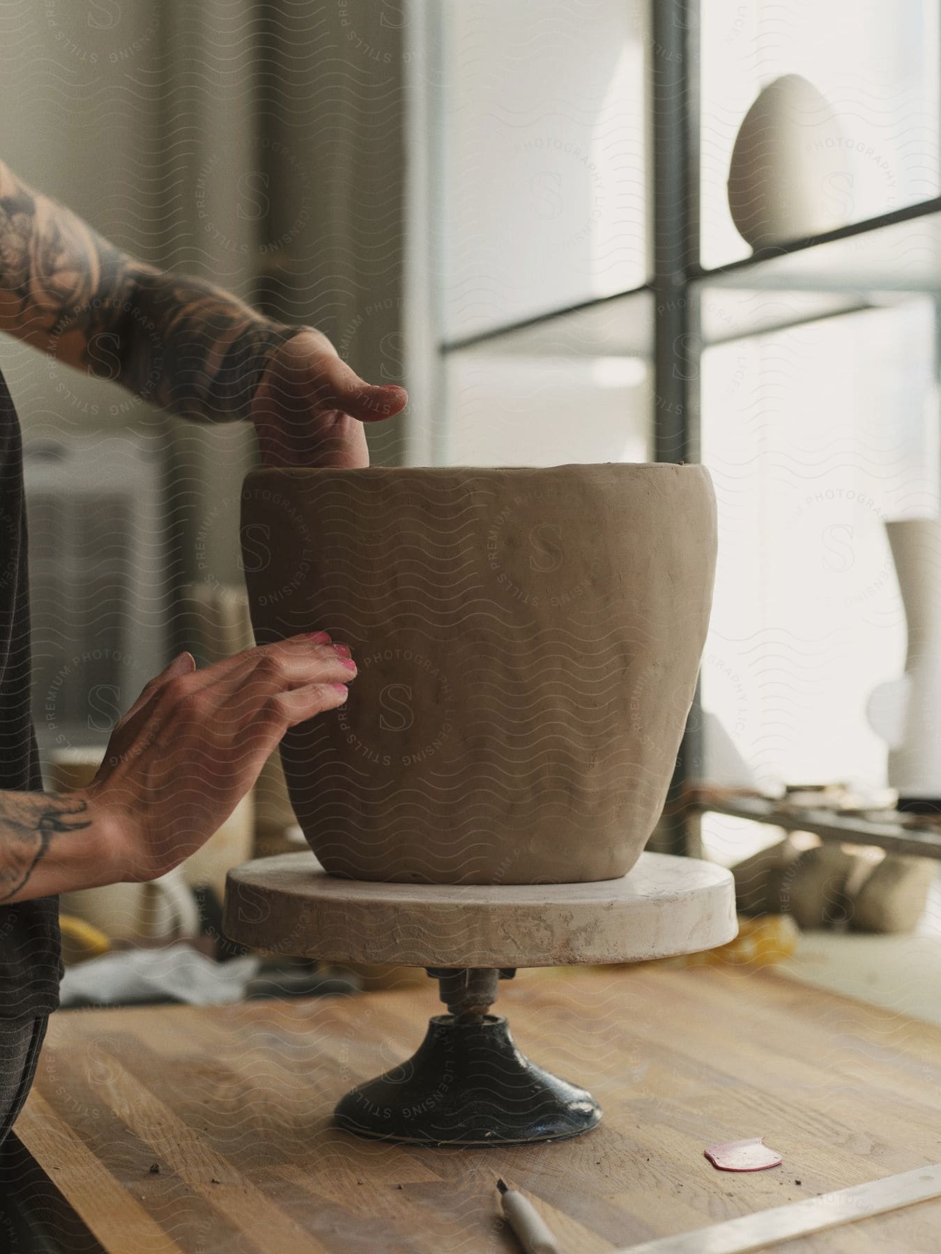 Stock photo of hands with pink nails and tattoos making pottery indoors