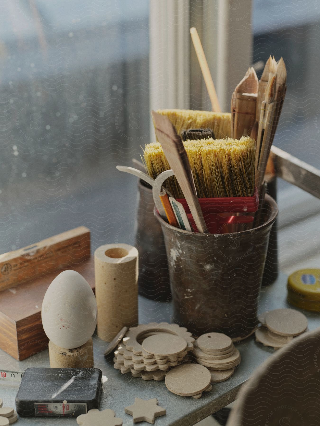 Paint brushes and tools in a canister next to wooden craft supplies and a tape measure on a table surface