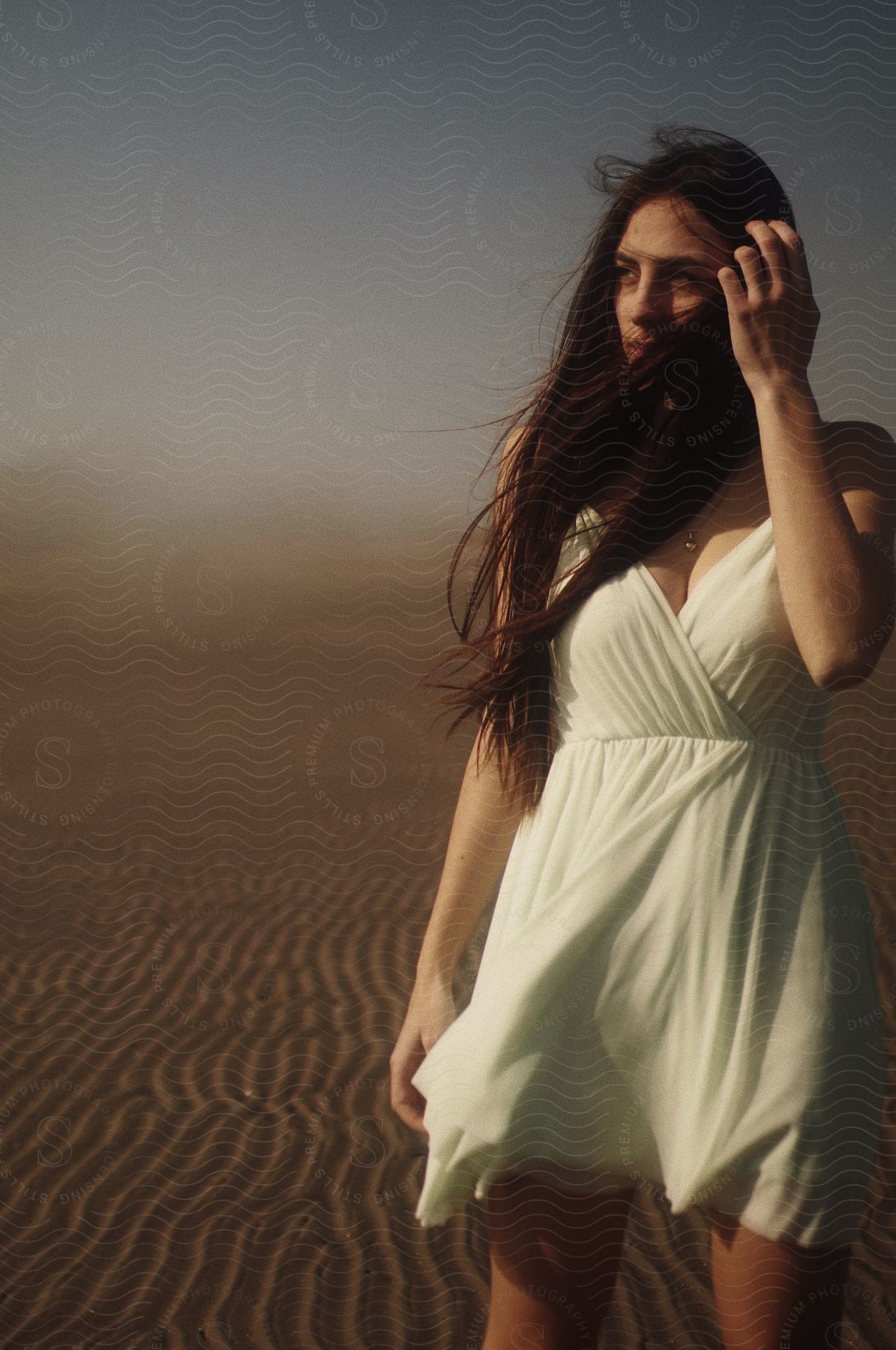 A woman with brown hair and white dress stands in the desert