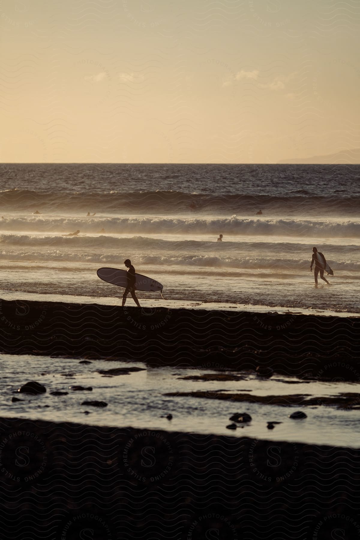 People carrying surfboards on the beach and swimming in the water as waves roll into shore