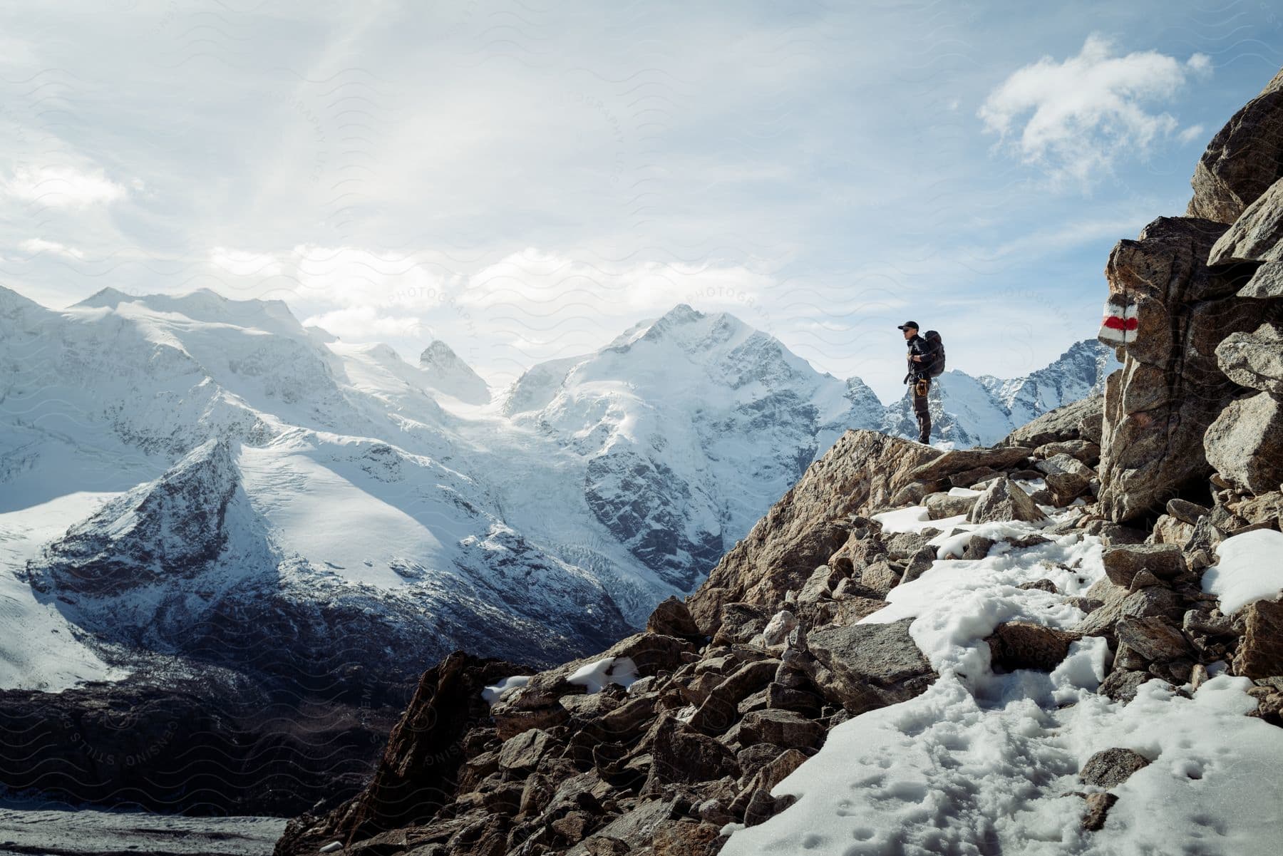 Man standing on a mountain peak surrounded by snowcapped mountains