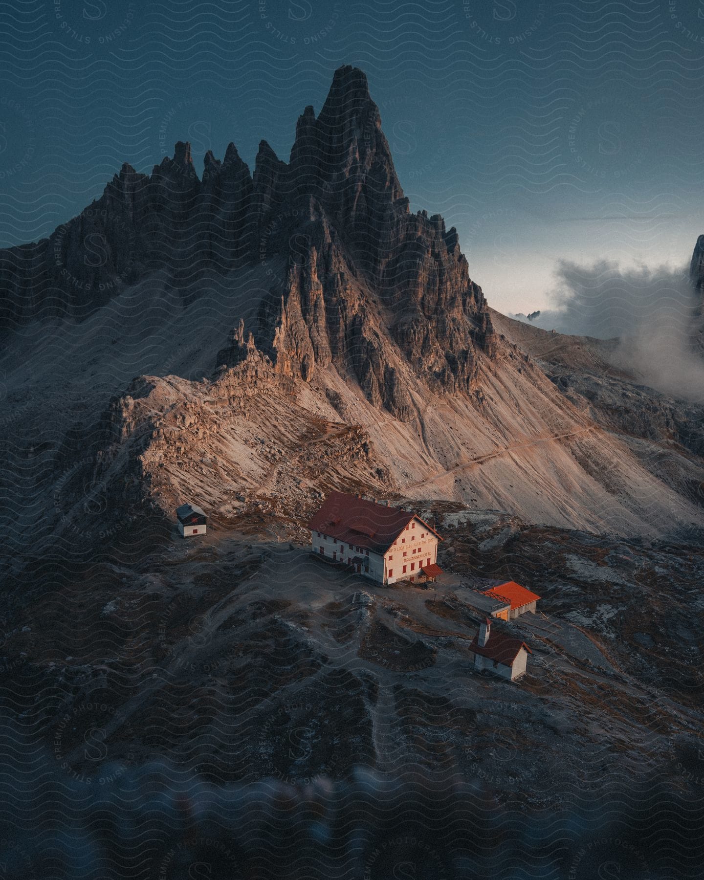 A Hotel With Three Adjacent Houses Below A Looming Mountain Peak