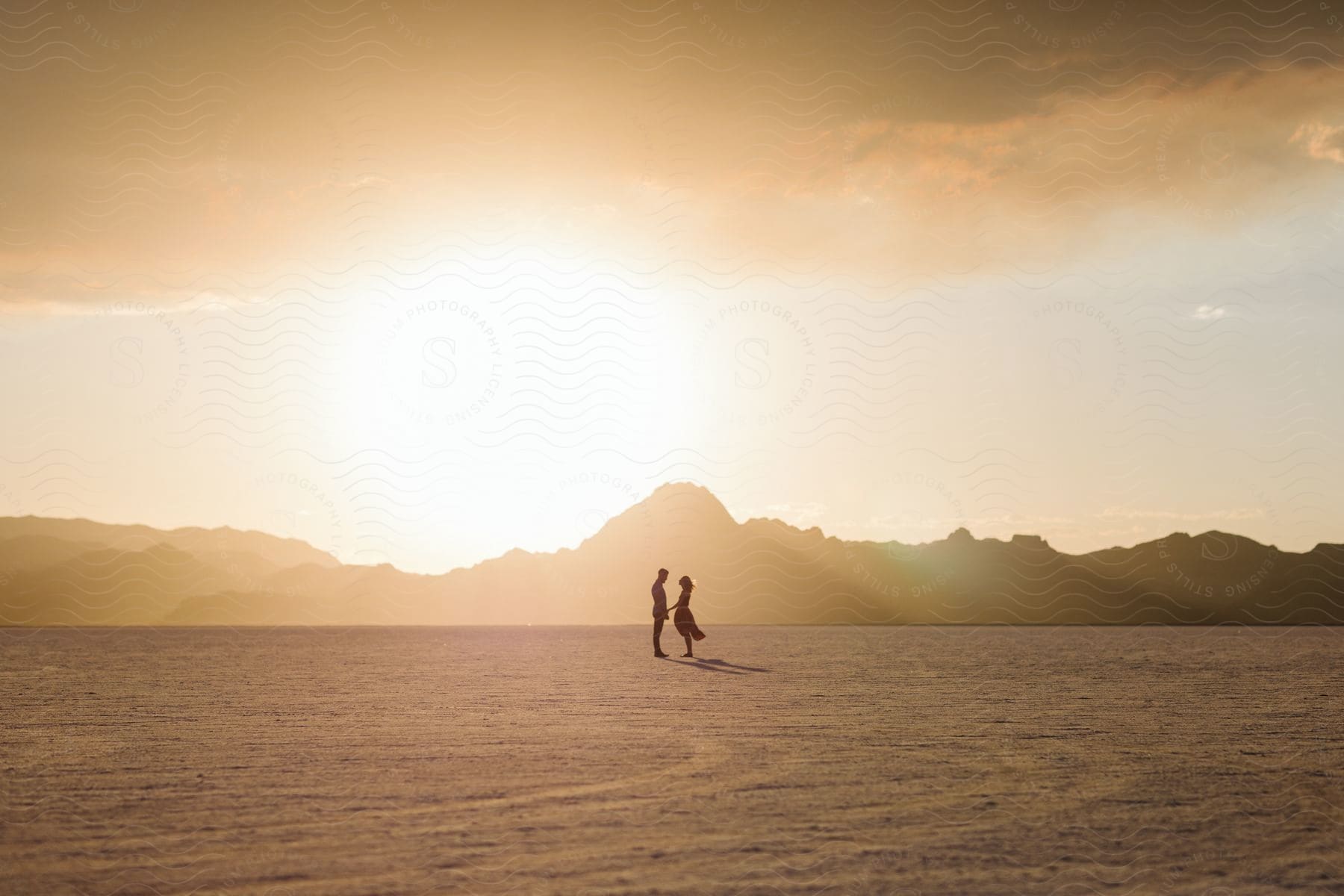 Stock photo of a romantic couple standing in a flat desert landscape with mountains on the horizon